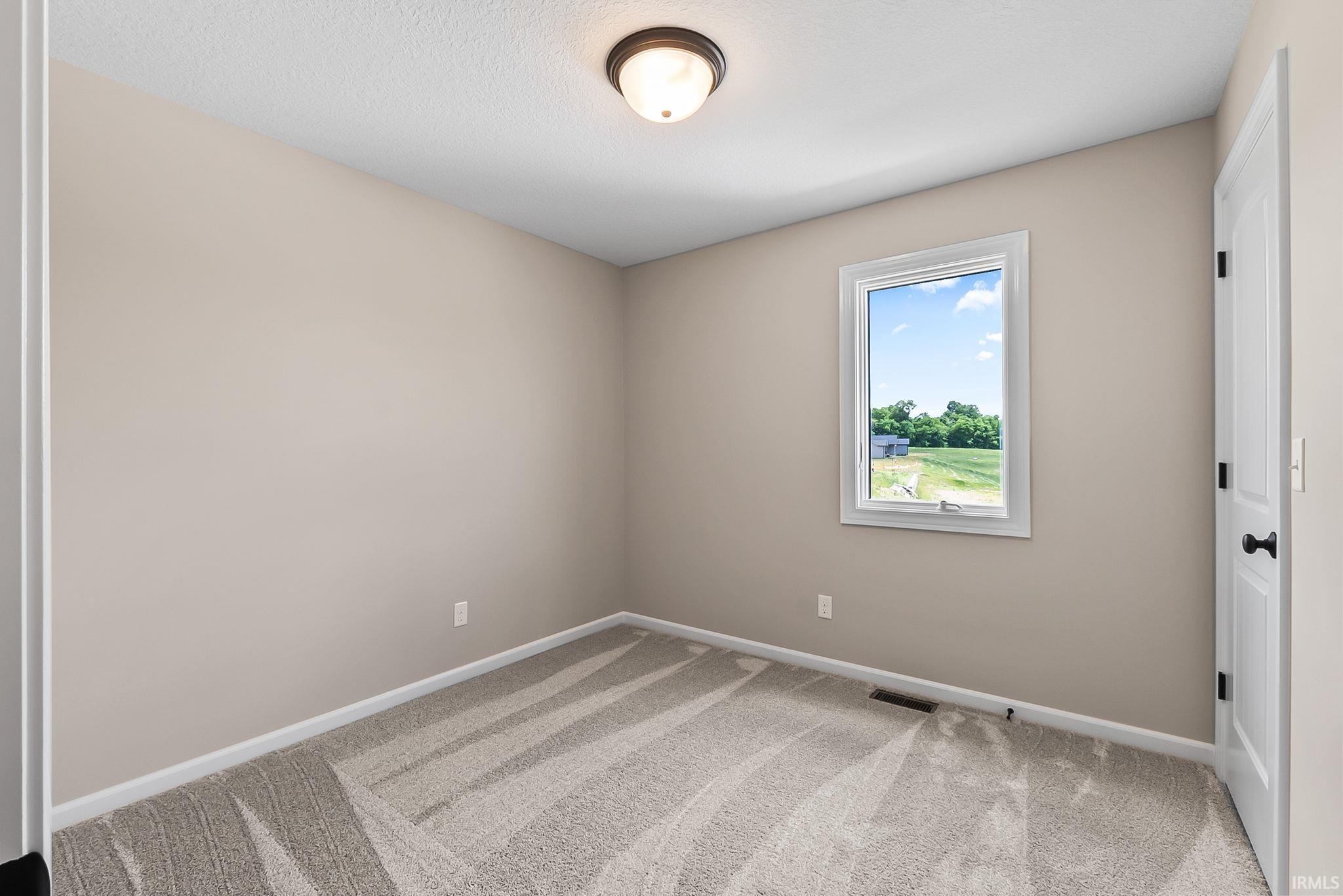 Neutral-toned room featuring light beige walls and patterned carpet flooring