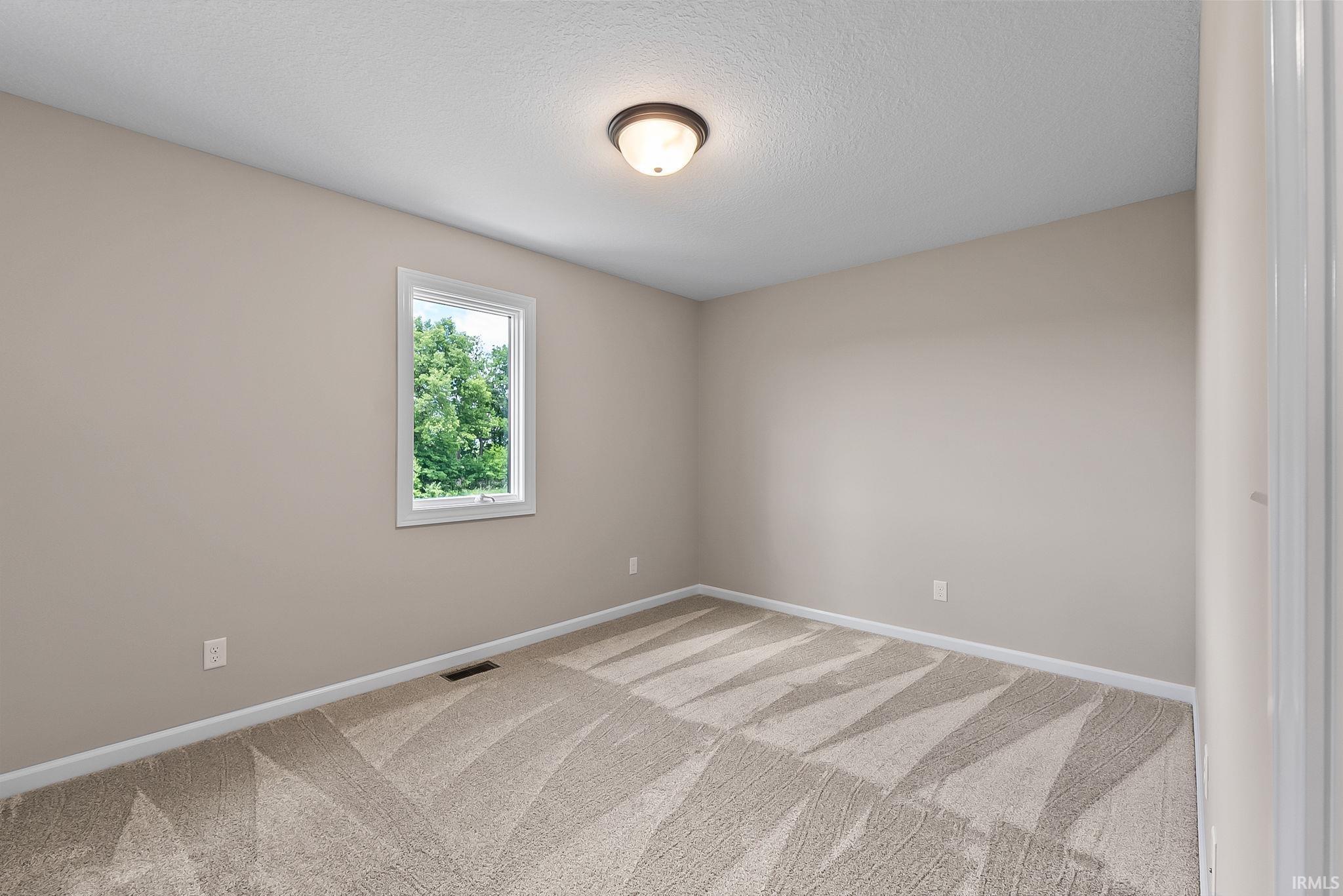 Neutral-toned room with patterned carpet flooring, a window offering natural light, and a flush mount ceiling light fixture