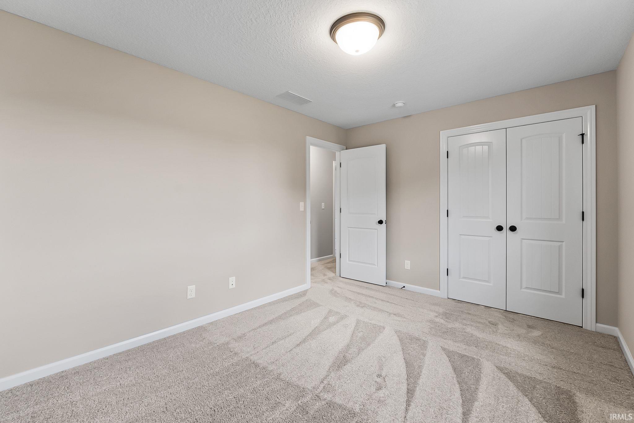 Spacious room featuring light-toned walls, white trim, and patterned carpeting
