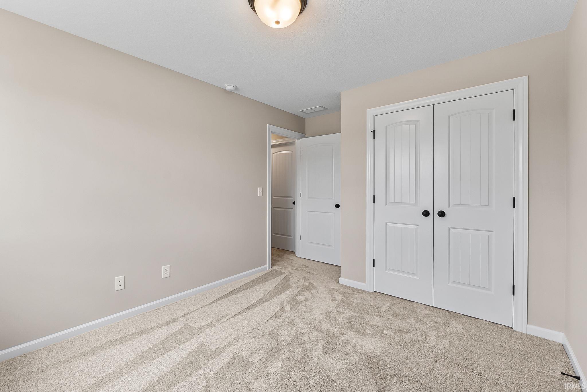 Neutral-toned walls and plush carpet flooring complement a pair of white paneled closet doors with black hardware