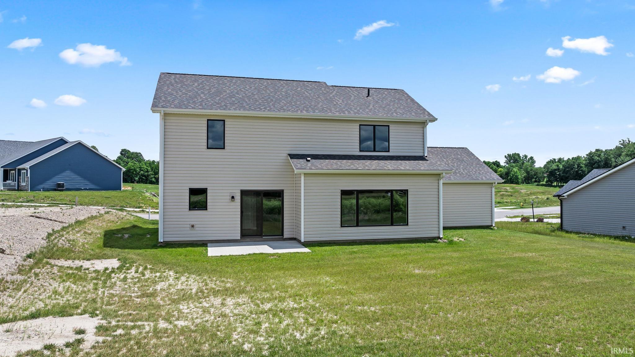 Rear exterior featuring light-colored siding, a dark shingle roof, and a ground-level concrete patio