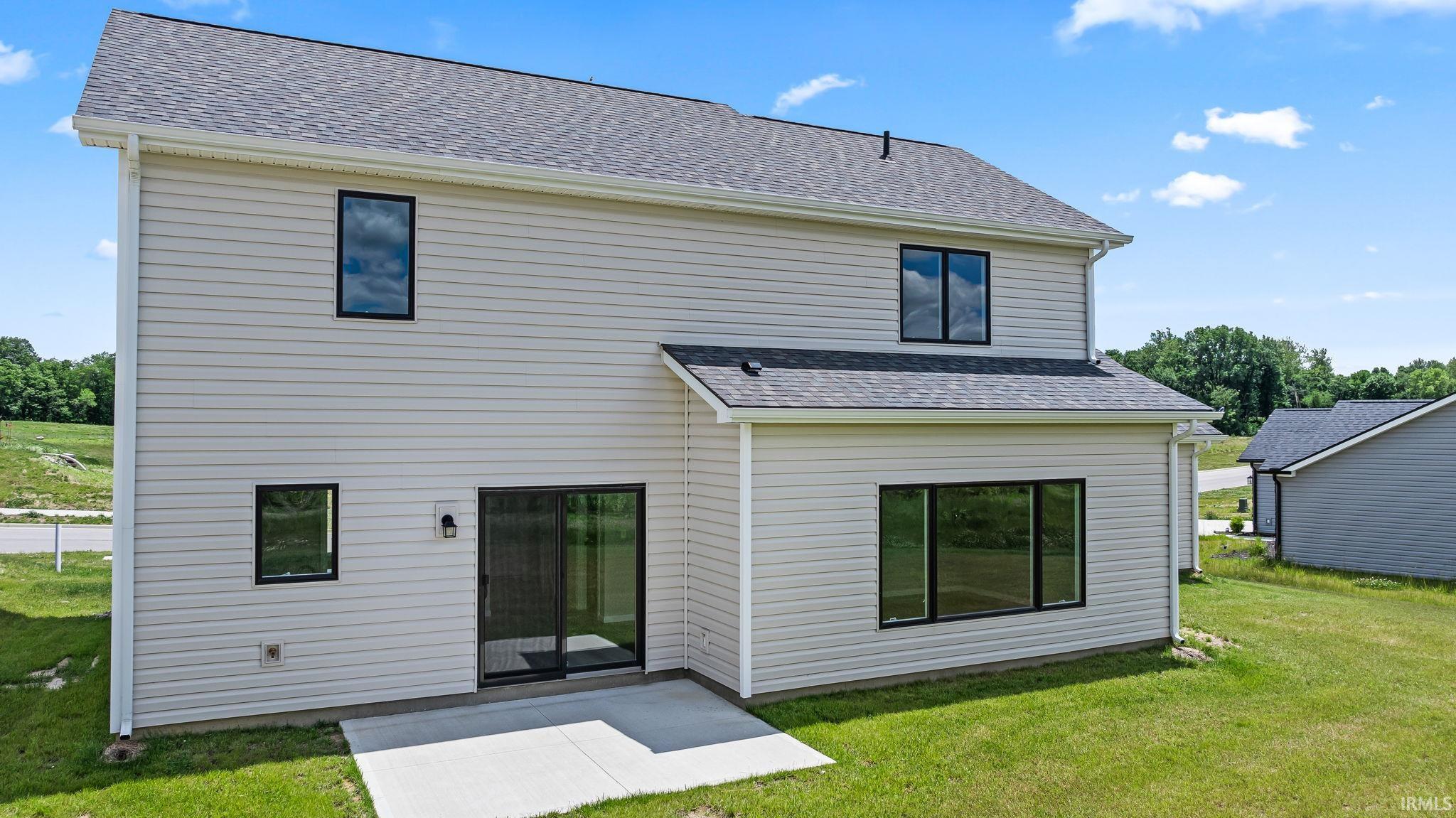 Rear exterior featuring light-colored horizontal siding, a dark shingle roof, and black-framed windows