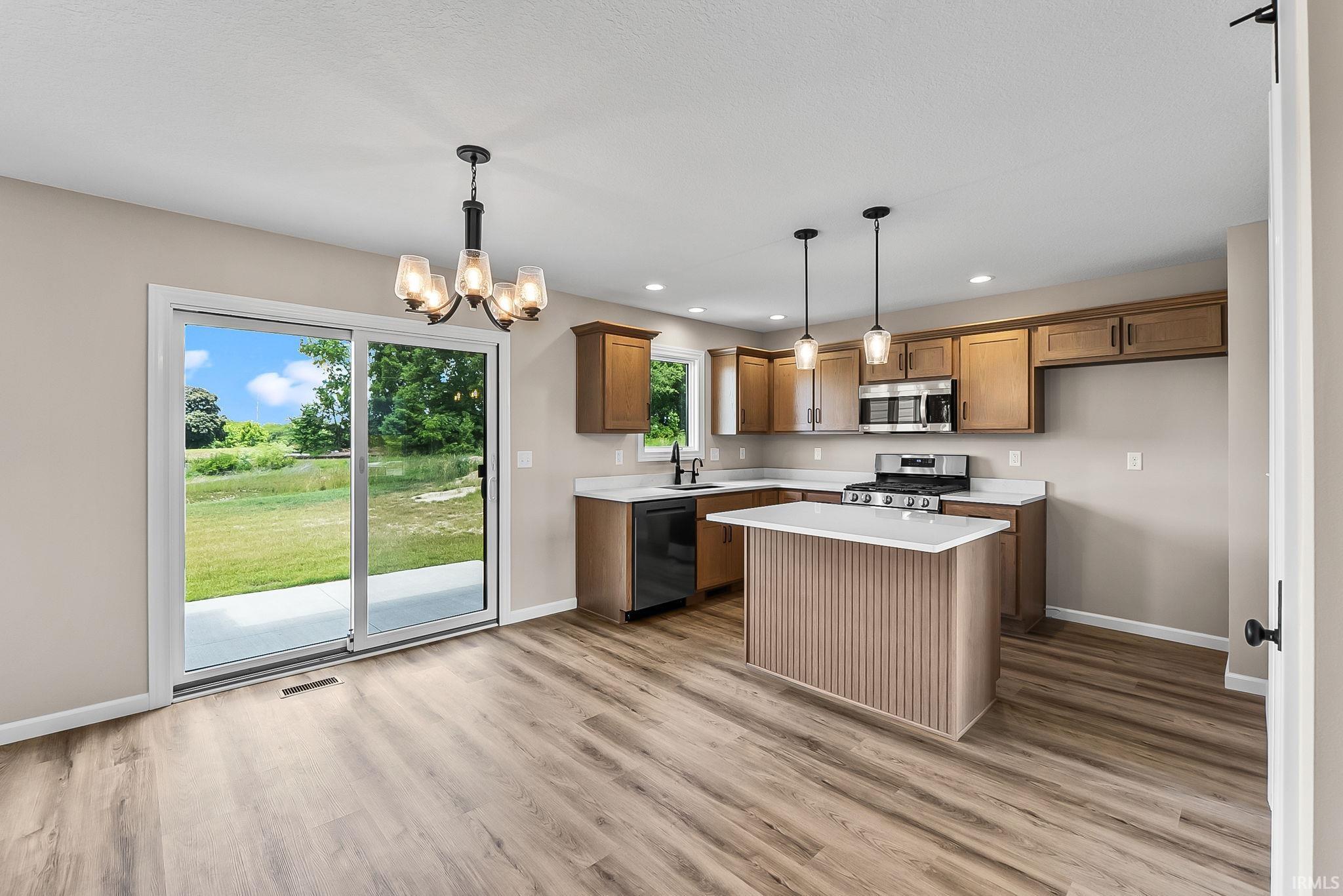 Open-concept kitchen with wood-finish flooring, featuring a central island with a white countertop, recessed lighting, and stainless steel appliances