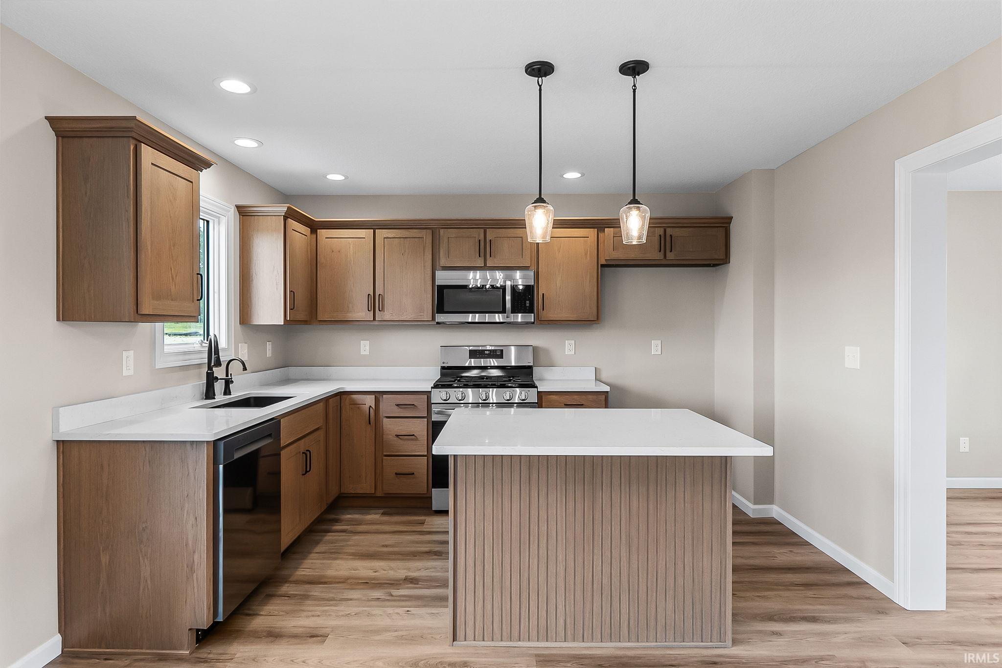 Modern kitchen featuring wood-finish cabinetry, stainless steel appliances, a center island with a white countertop, recessed lighting, and wood-finish flooring