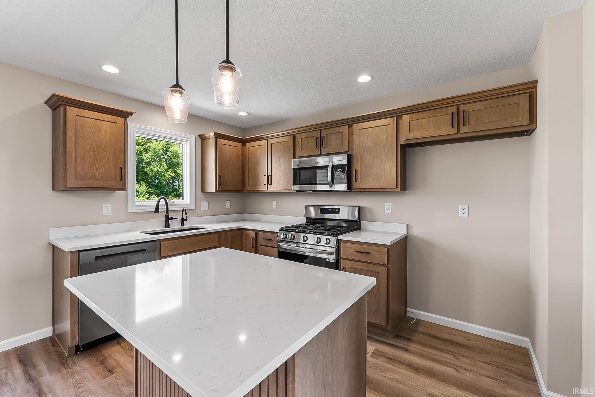 Kitchen featuring a central island with a white countertop, wood-finish flooring, wood cabinetry, stainless steel appliances, and recessed lighting