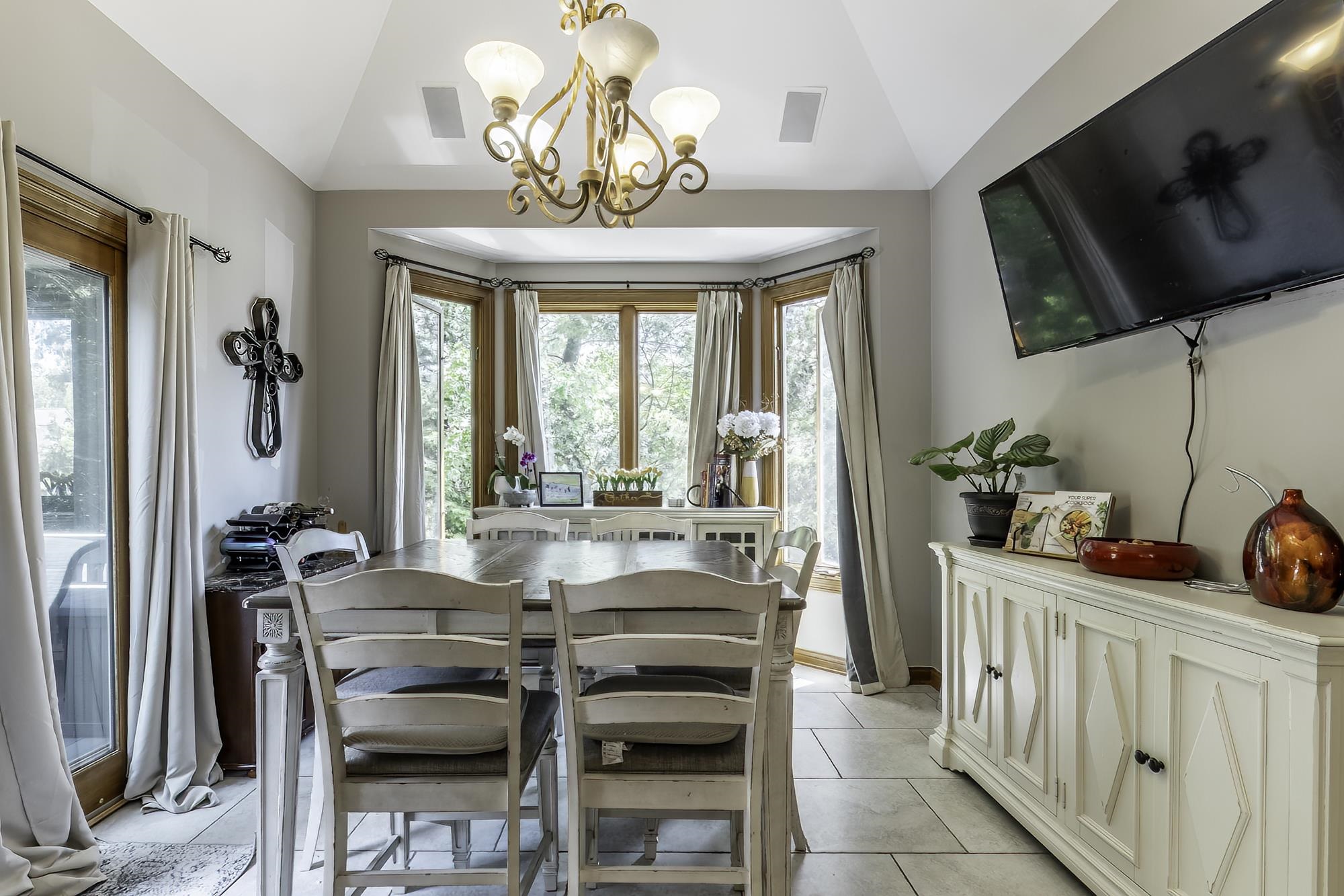 Dining area featuring a vaulted ceiling with a chandelier, a bay window with wood trim, a glass-paned exterior door, and large format tile flooring