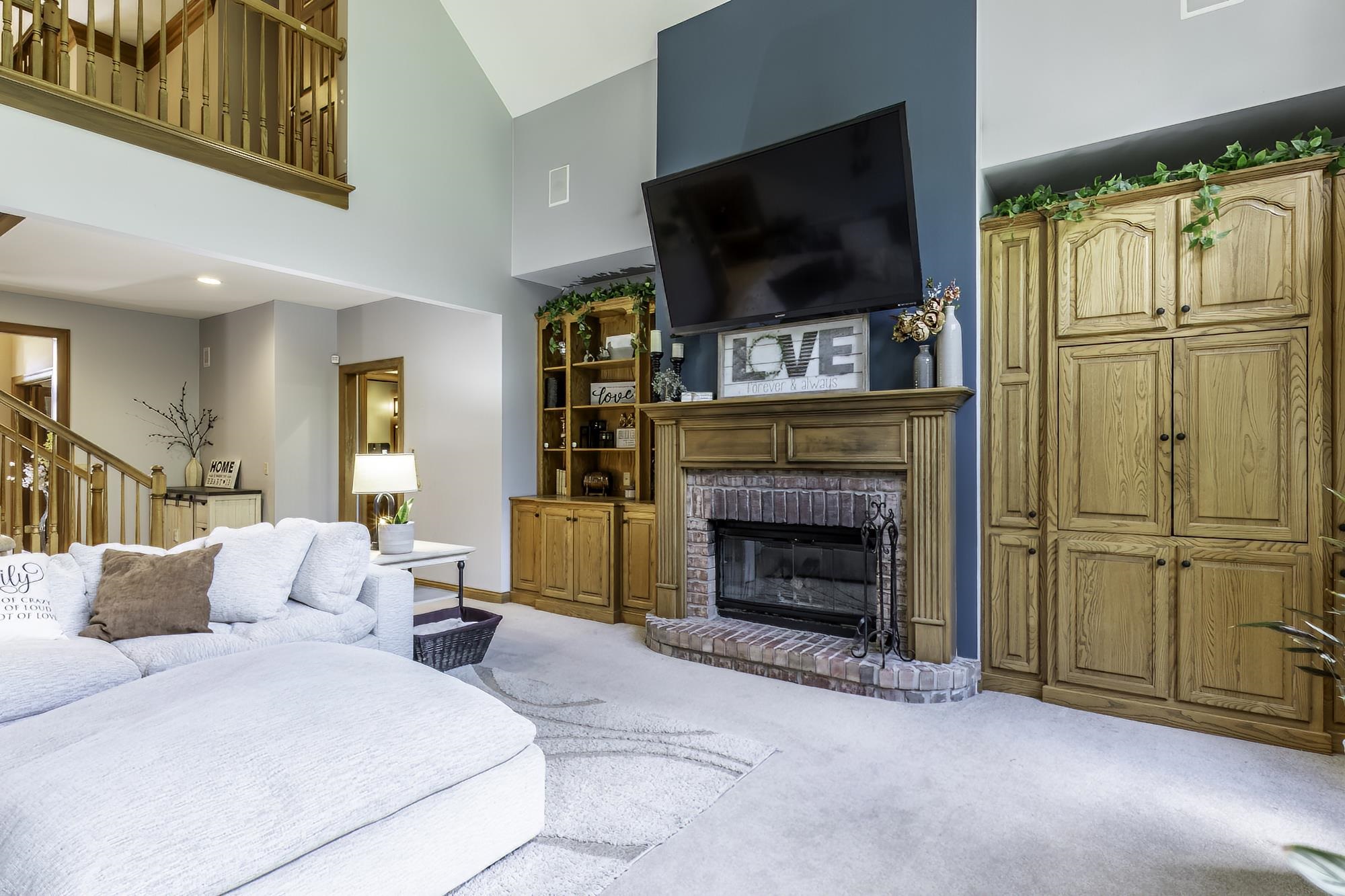 Living area featuring a floor-to-ceiling brick fireplace with a wood mantel, built-in wooden cabinetry, and carpeting
