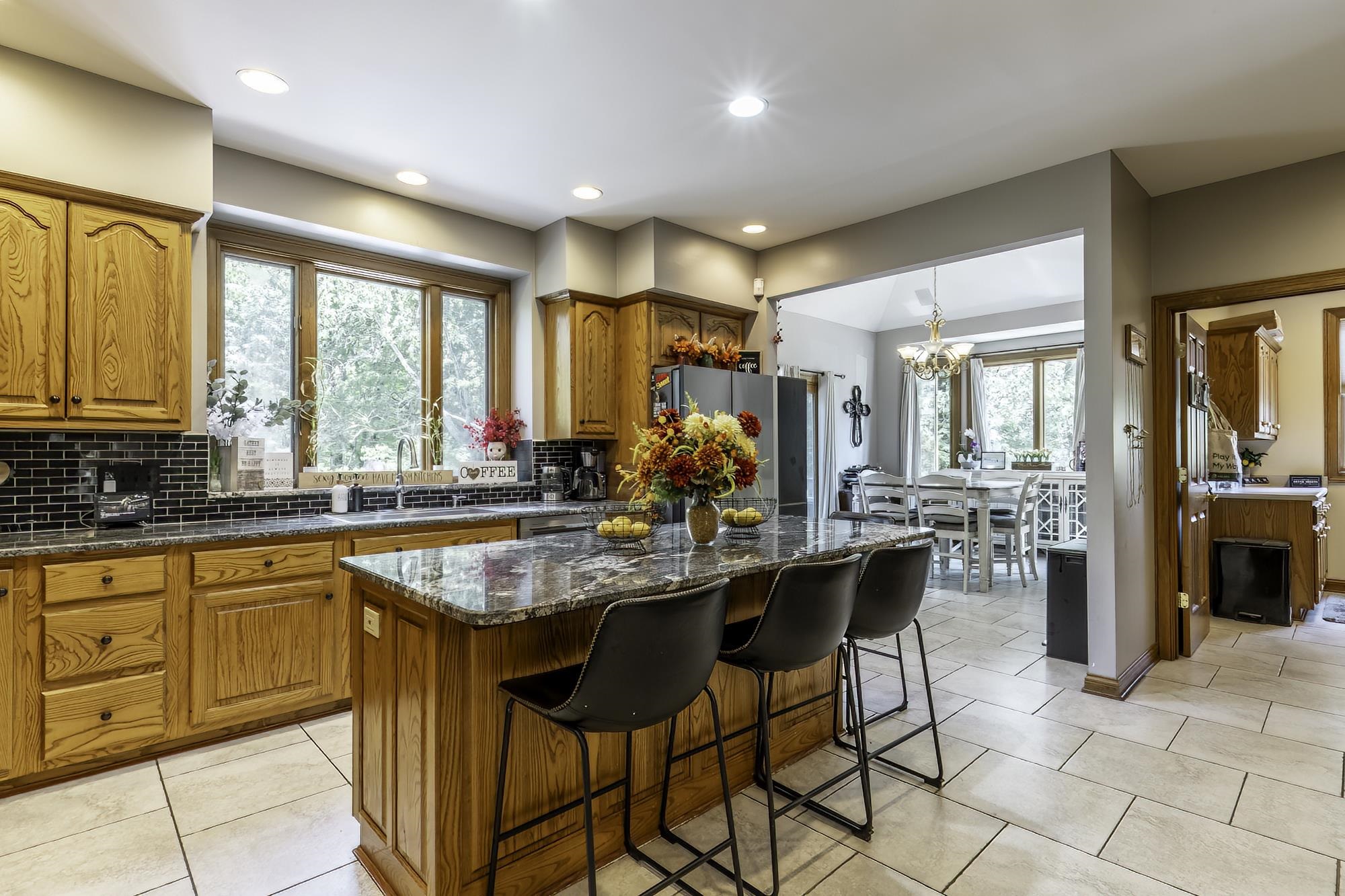 Spacious kitchen featuring wood cabinetry, dark backsplash, and a central island with a stone countertop