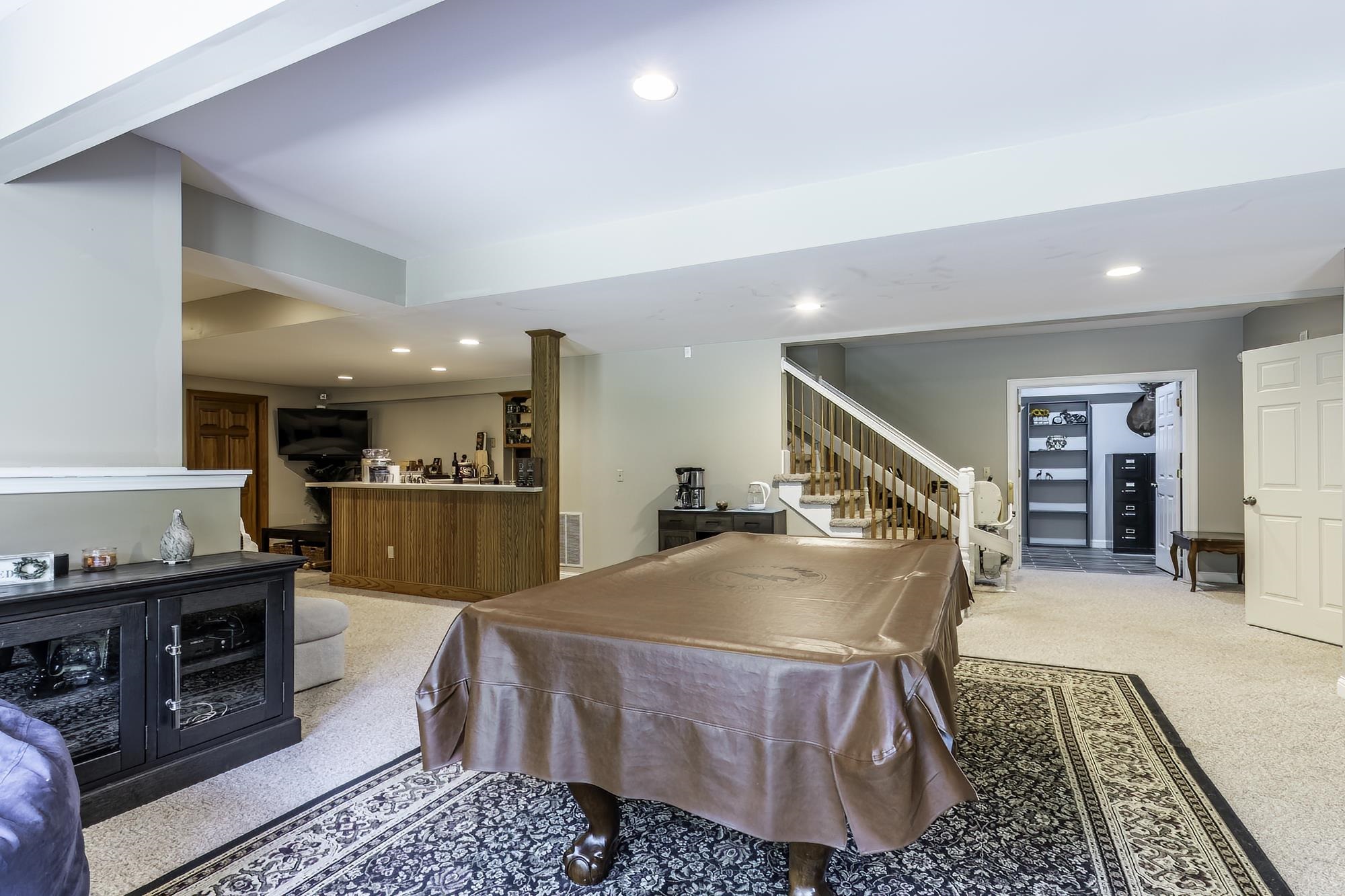 Spacious finished basement featuring recessed lighting, a built-in wood-finish bar, carpeted flooring, and a staircase with wood railings