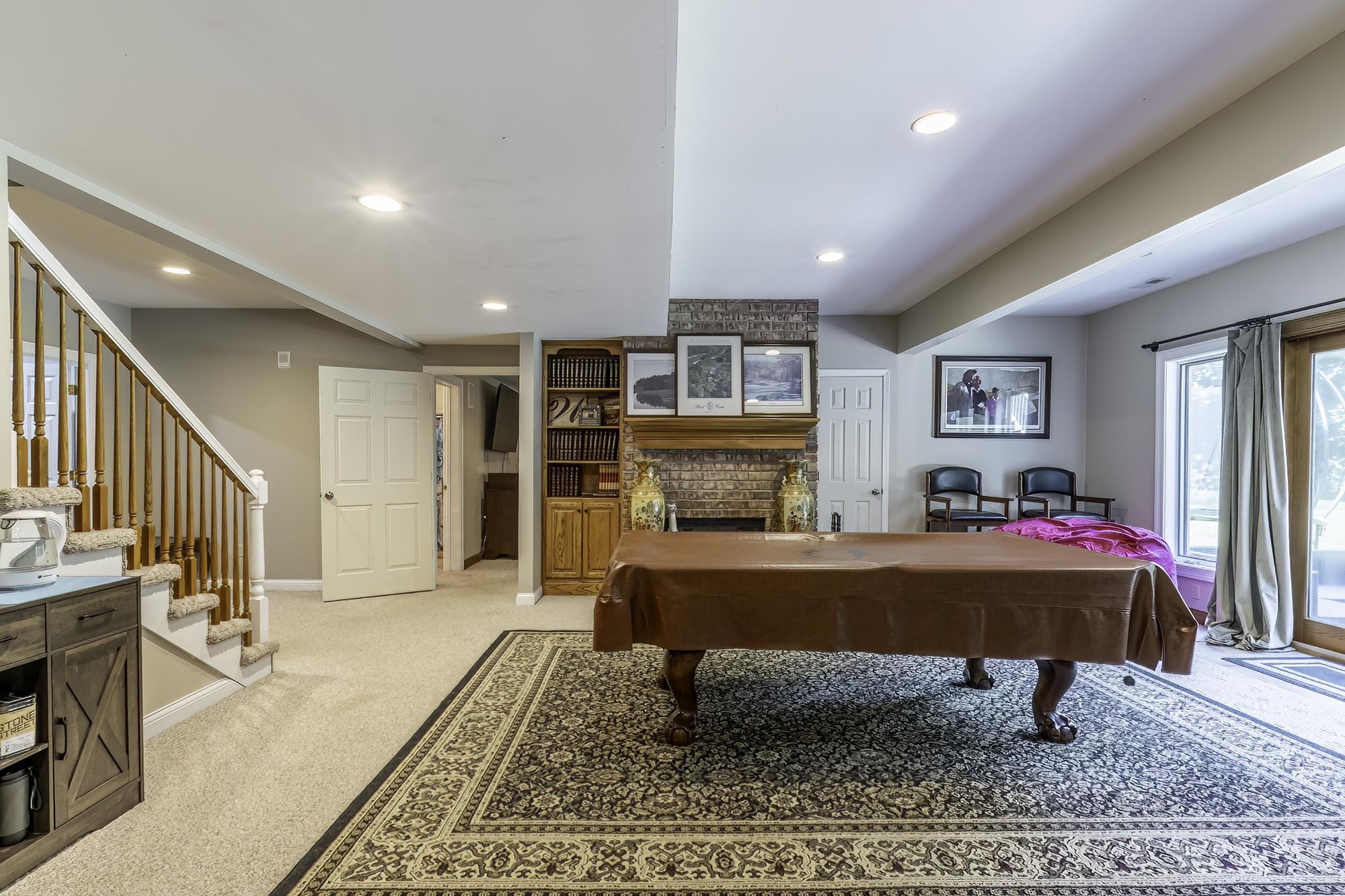 Finished lower level featuring recessed lighting, a brick fireplace with wood mantel, built-in shelving, and direct exterior access through glass-paned doors