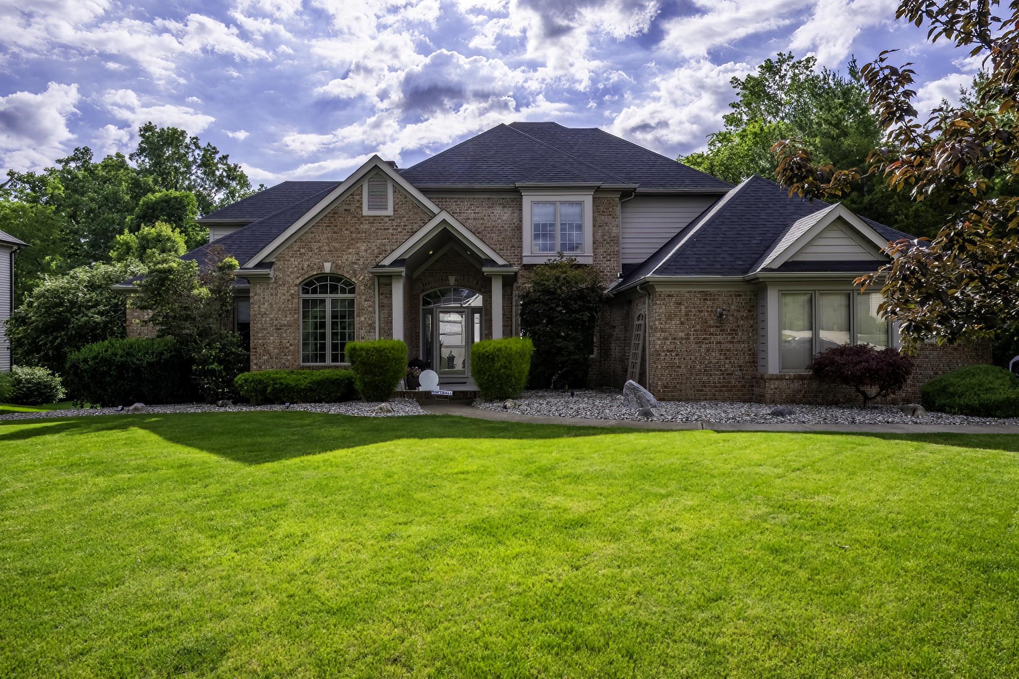 Traditional brick exterior featuring a prominent gabled entry, multiple window styles including an arched palladium, and a dark shingle roof