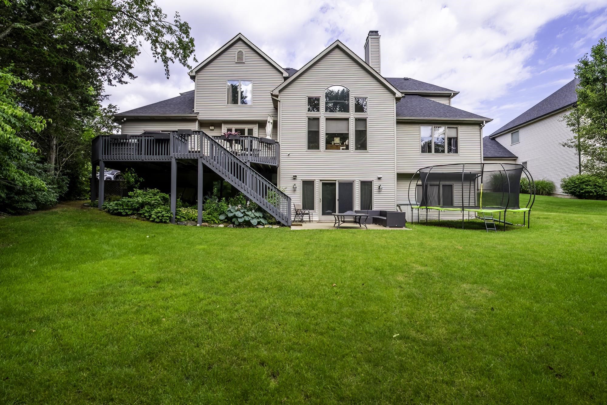 Expansive backyard featuring a large green lawn, multi-level composite deck, ground-level patio, and mature perimeter trees