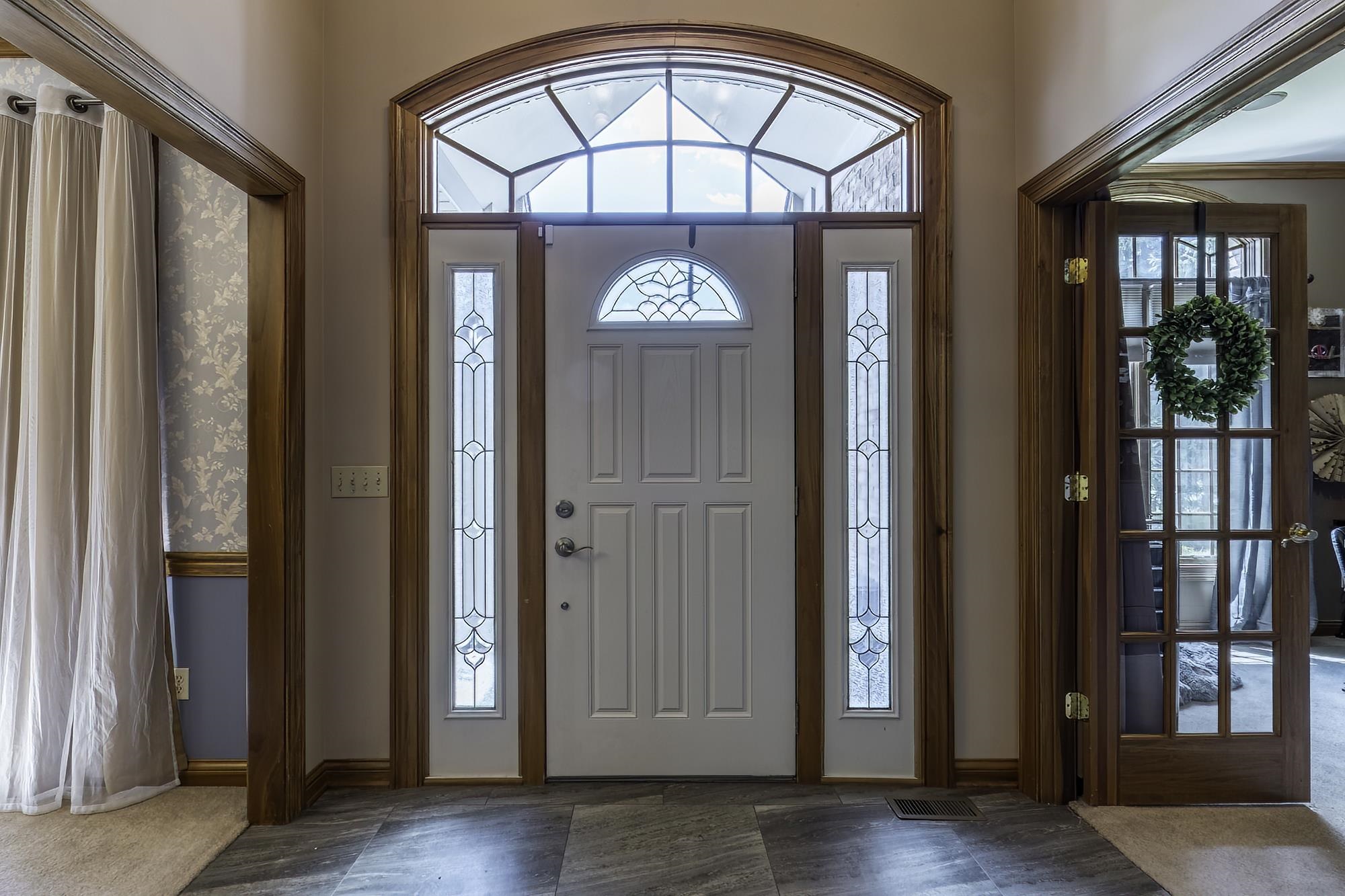 Grand entryway featuring a white paneled front door with decorative glass, flanked by two sidelights with matching intricate glasswork