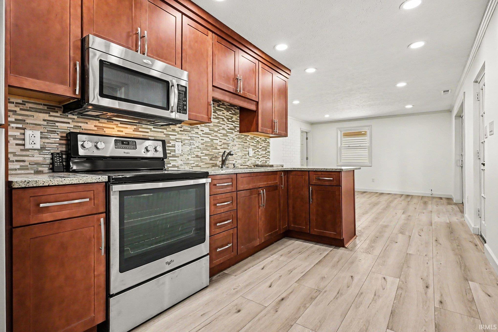 Kitchen featuring wood-finish cabinetry, stainless steel appliances, speckled countertops, a mosaic tile backsplash, and recessed lighting