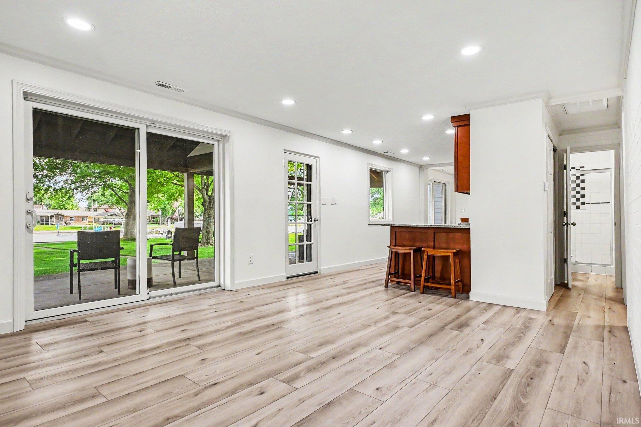 Spacious interior featuring wood-finish flooring, sliding glass doors to outdoor patio, recessed lighting, white wall finishes, and a built-in bar with wood-finish cabinetry
