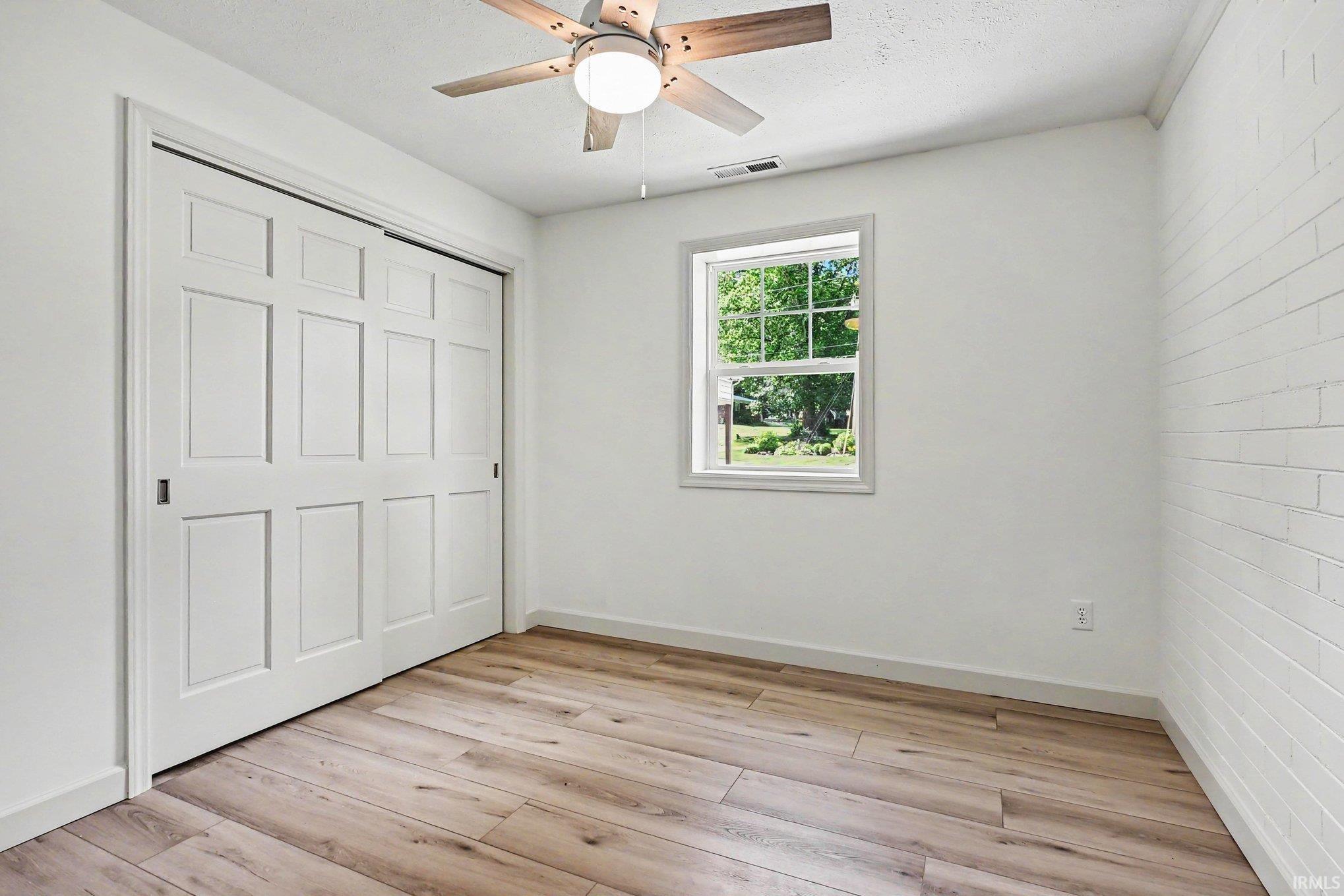 Bright room featuring wood-finish flooring, a white trim window, and a ceiling fan with light fixture