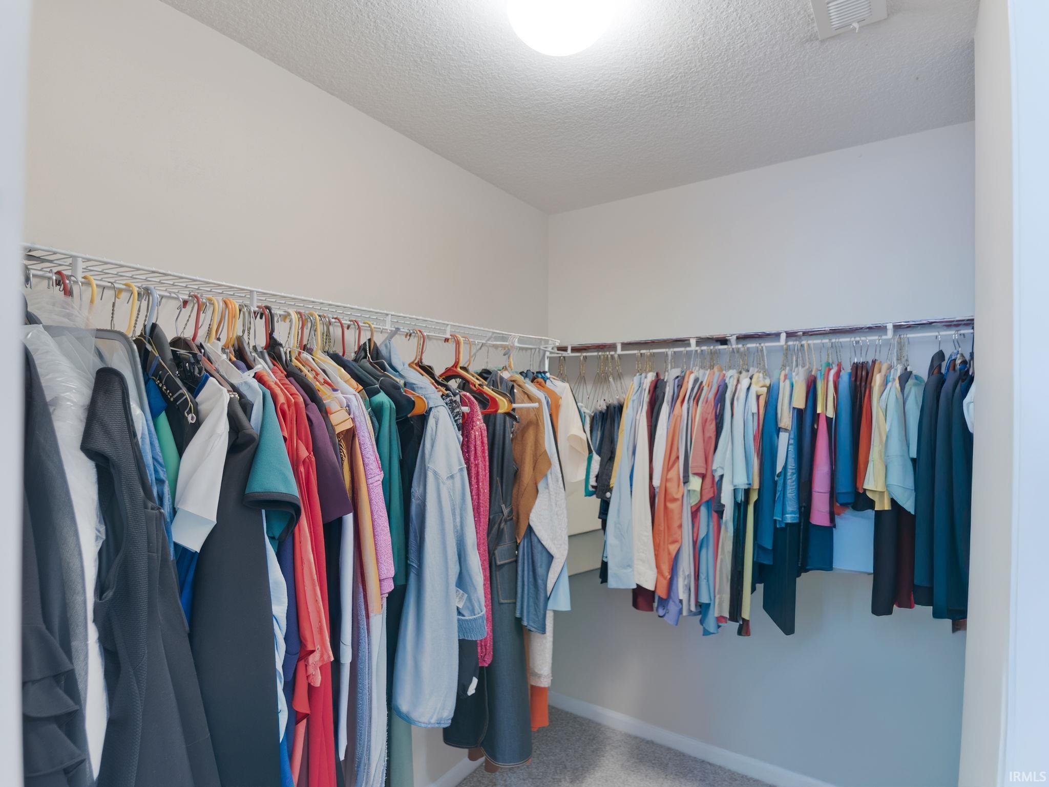 Spacious walk-in closet featuring light-toned walls, white wire shelving, and overhead lighting