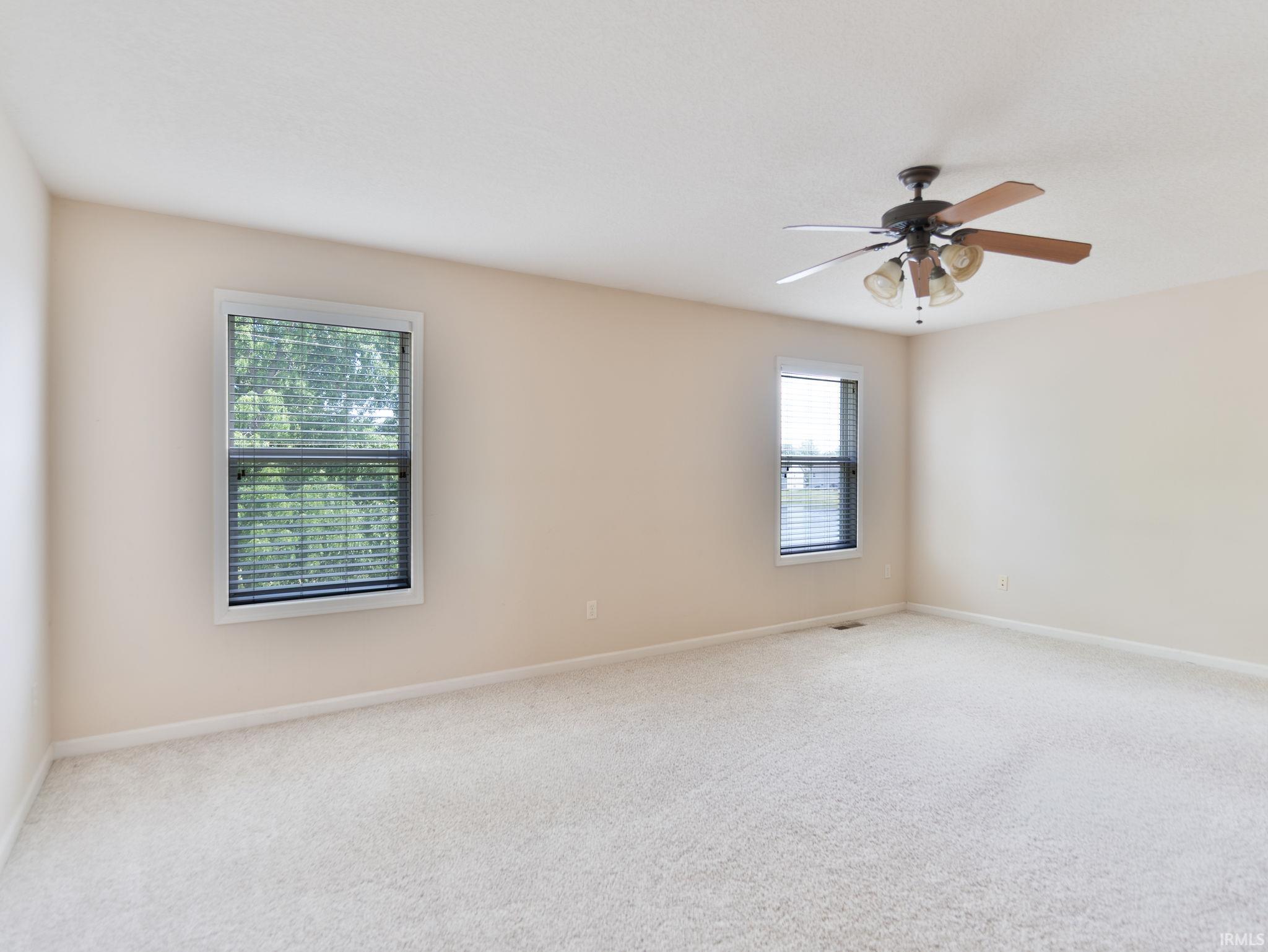 Carpeted interior room featuring two windows with blinds, a ceiling fan with integrated lighting, and neutral wall tones