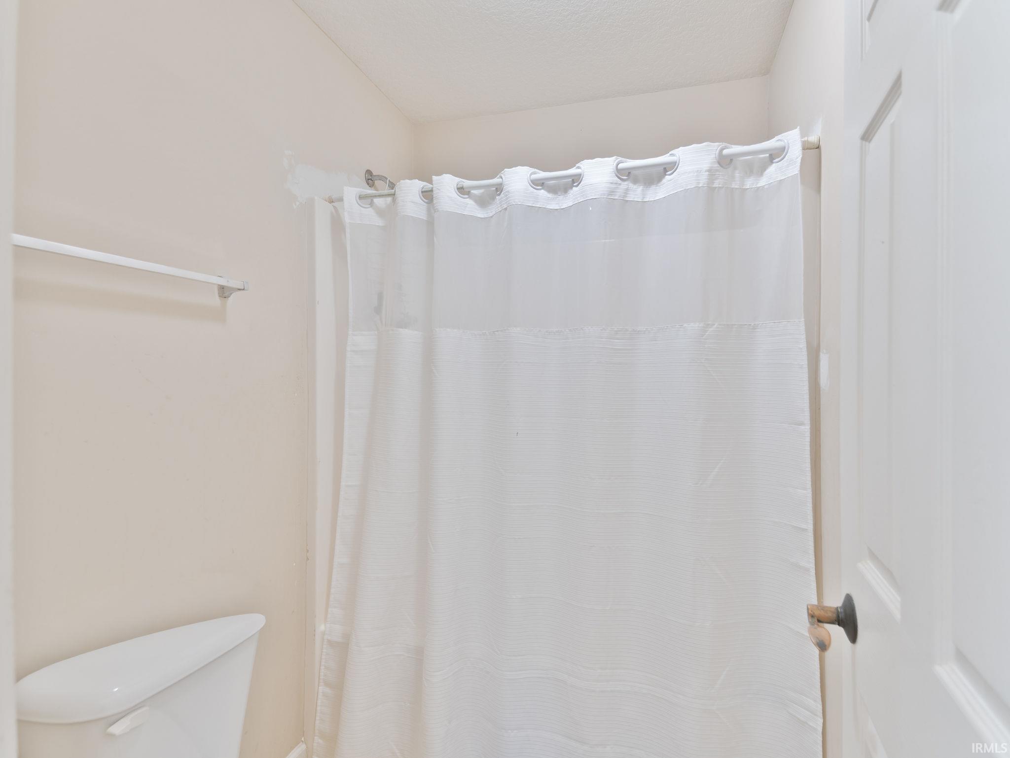 Bathroom featuring a white shower curtain on a curved rod, a white toilet fixture, and a towel bar