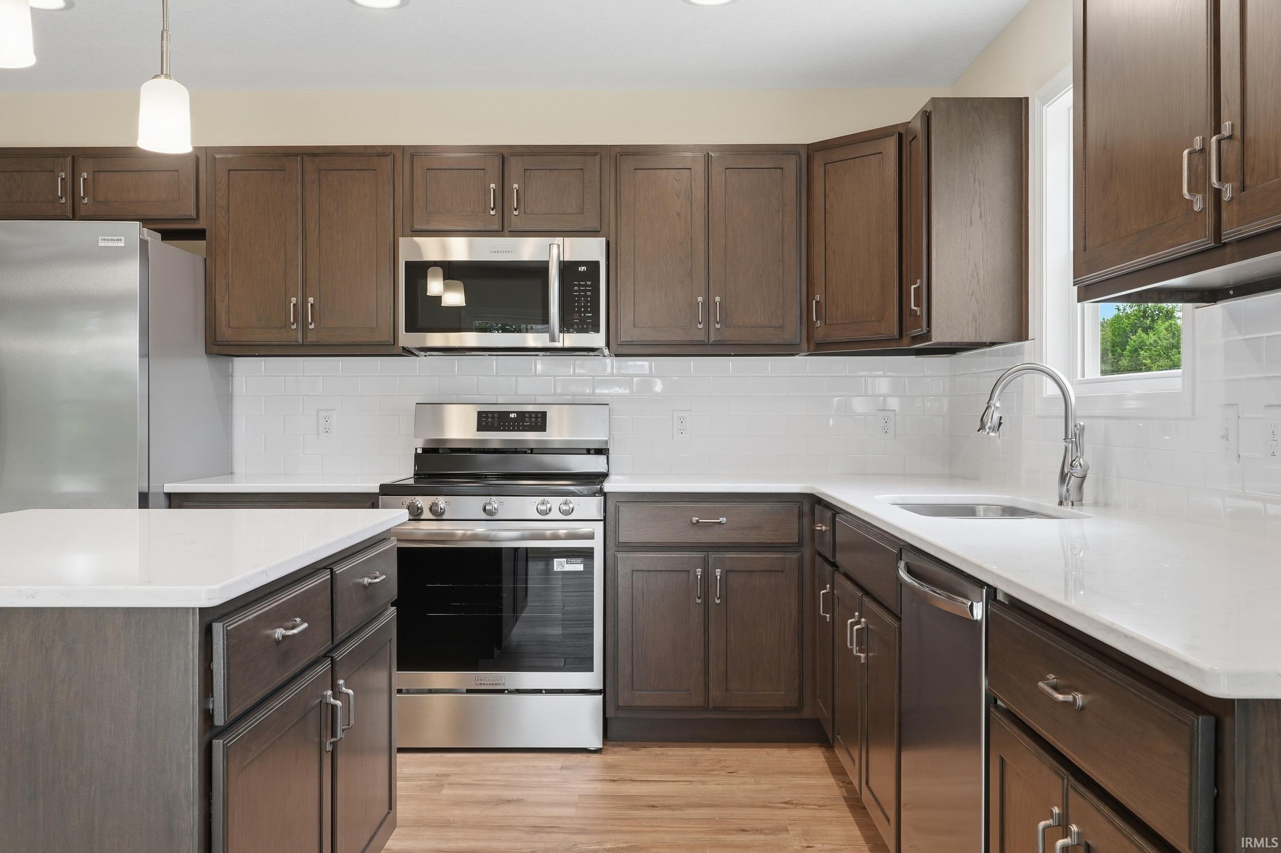 Kitchen featuring dark wood-finish cabinetry, stainless steel appliances, white subway tile backsplash, and light-toned countertops