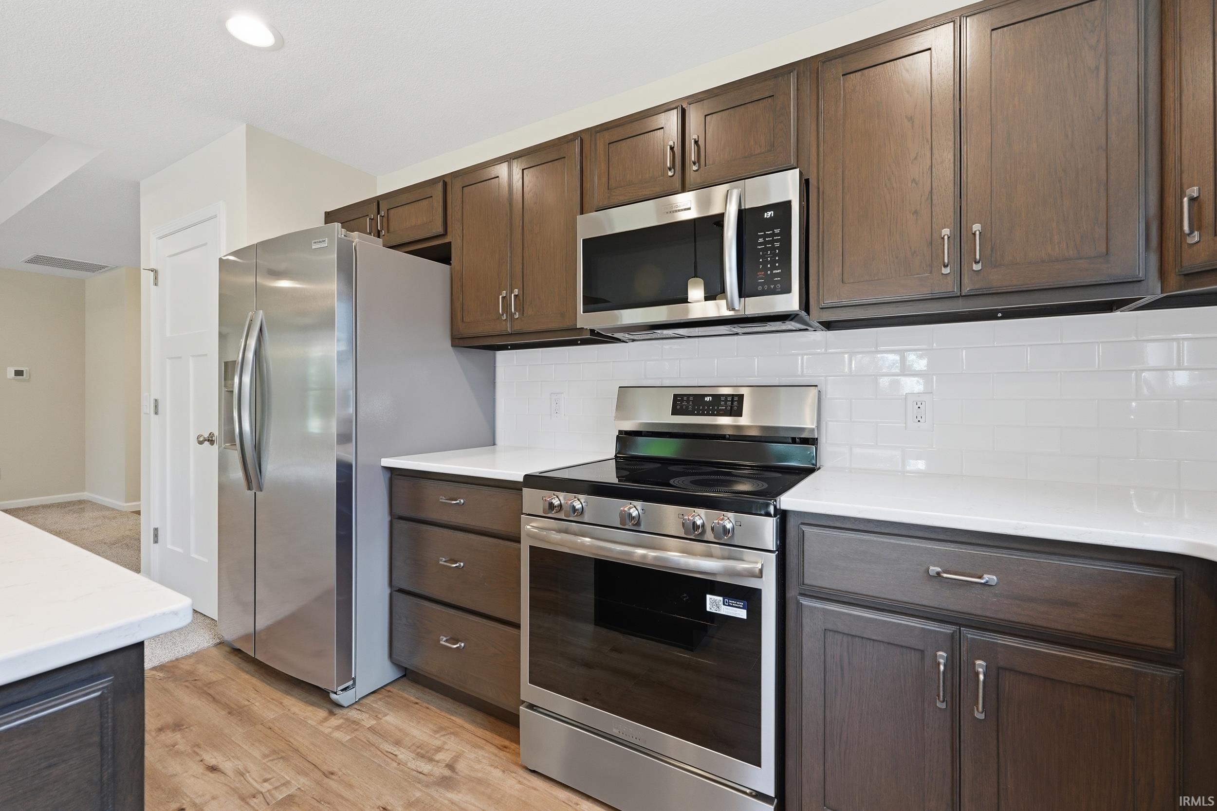 Kitchen featuring wood-finish flooring, dark wood cabinetry, white countertops, and a white subway tile backsplash