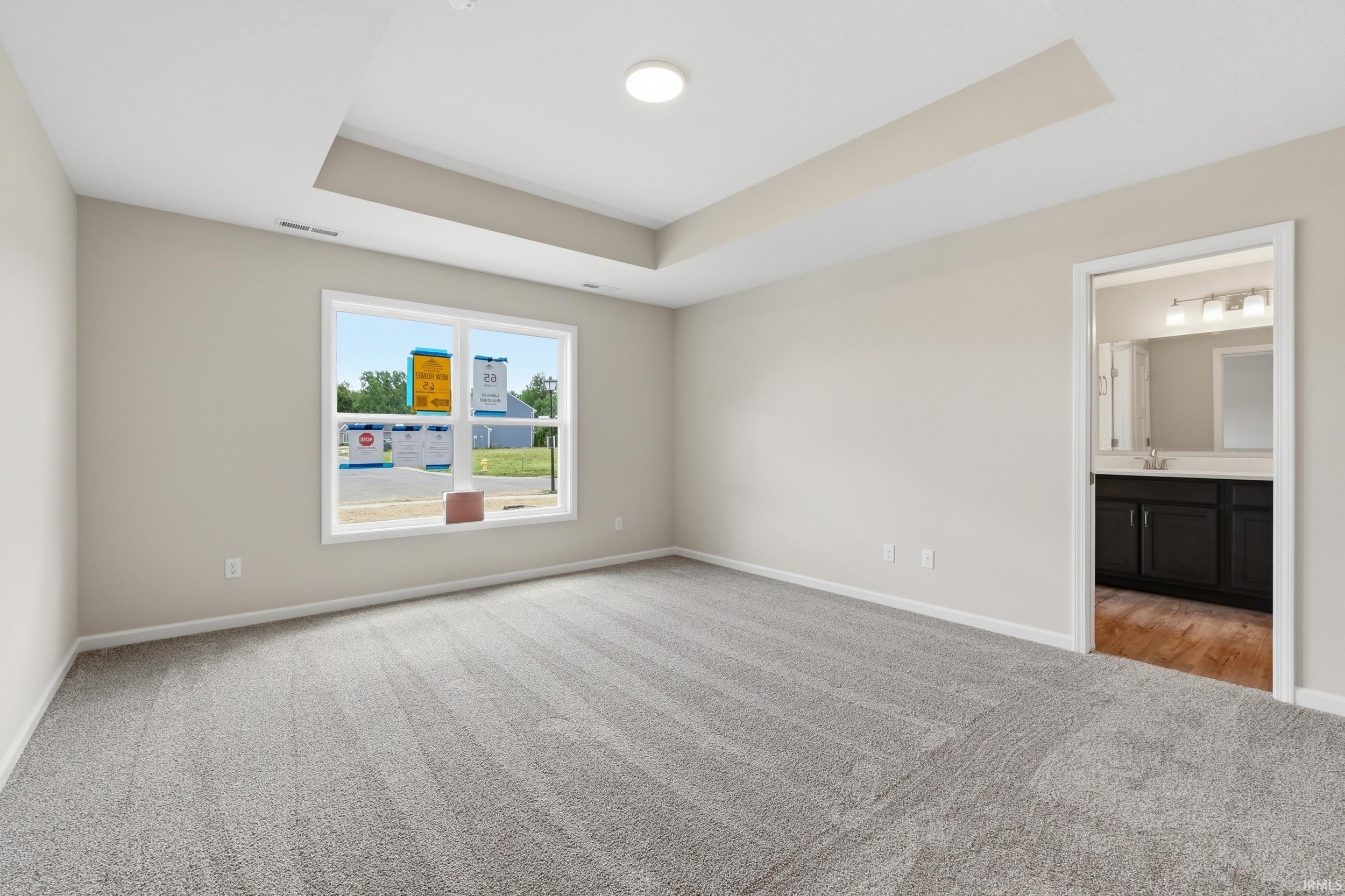 Spacious room featuring a tray ceiling with recessed lighting, light gray carpeting, and a large window