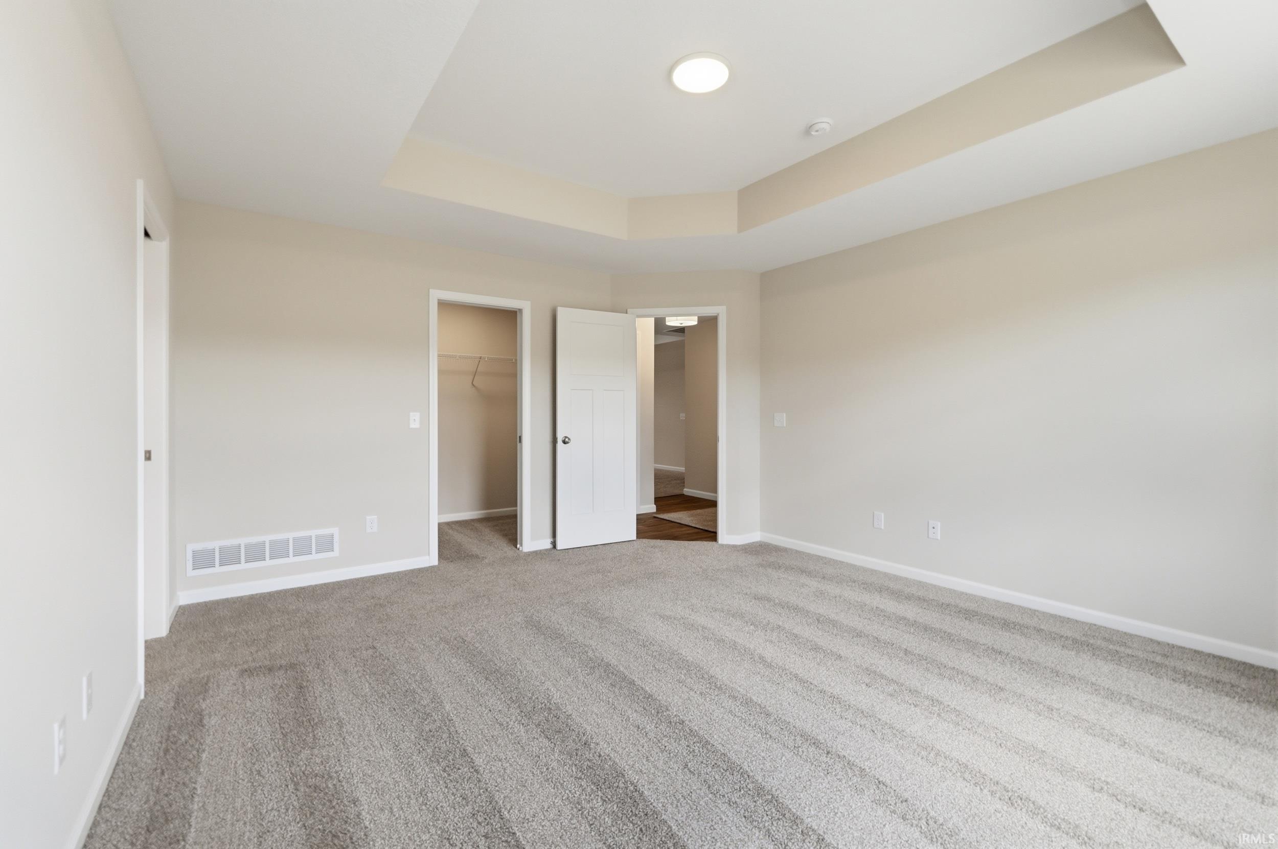 Spacious carpeted room featuring a tray ceiling with recessed lighting, an open doorway, and a closet with built-in shelving