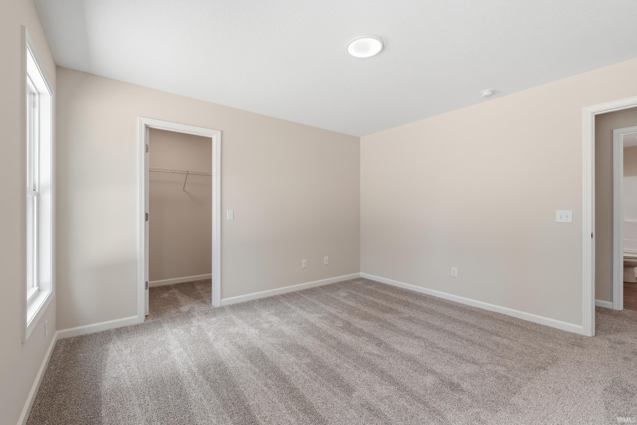 Room featuring neutral wall tones, gray carpeting, a window with white trim, and a built-in closet with wire shelving