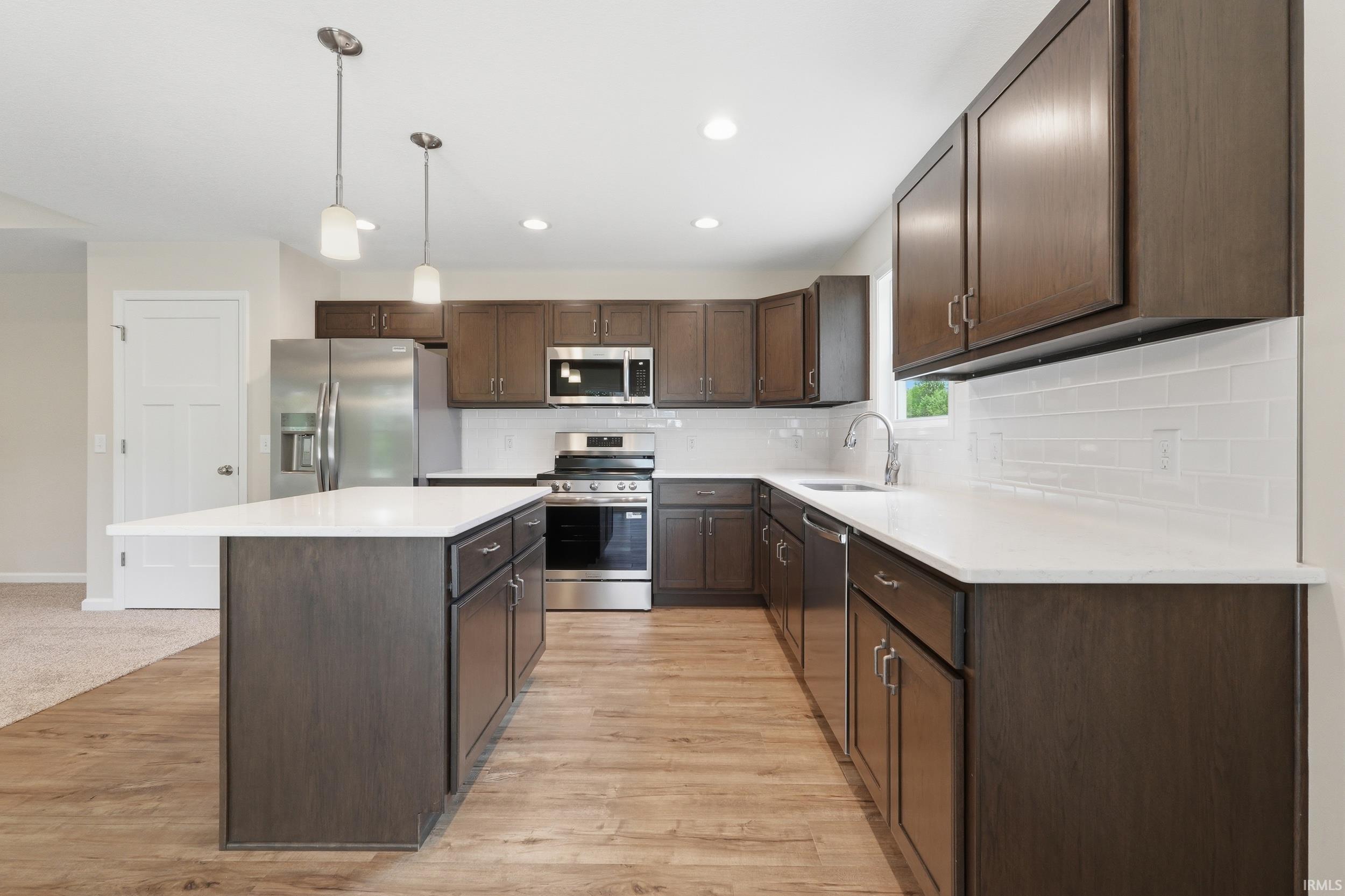 Kitchen featuring wood-finish flooring, dark wood cabinetry, white countertops, and stainless steel appliances