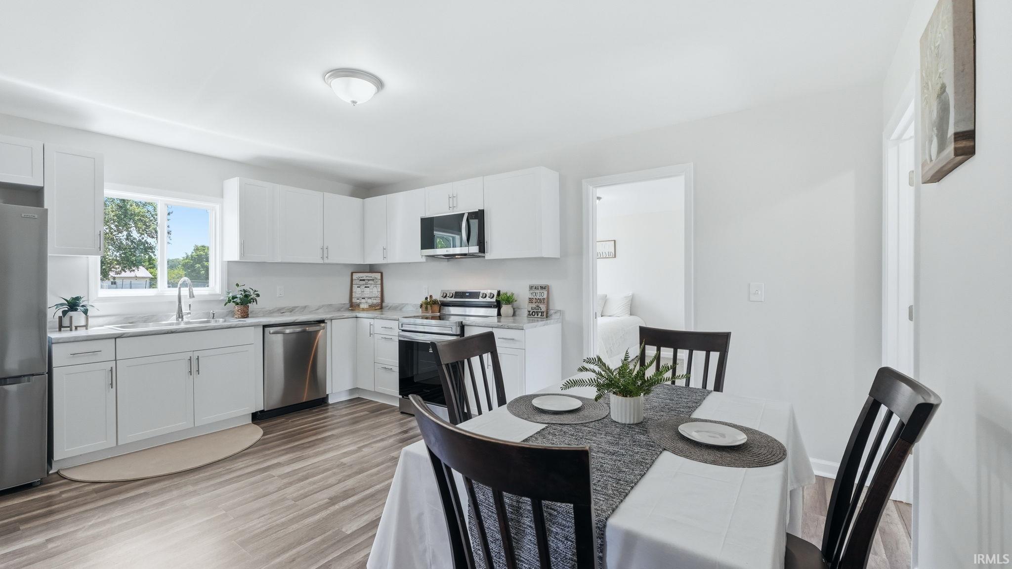 Open-concept kitchen featuring white cabinetry, stainless steel appliances, stone-finish countertops, and wood-finish flooring