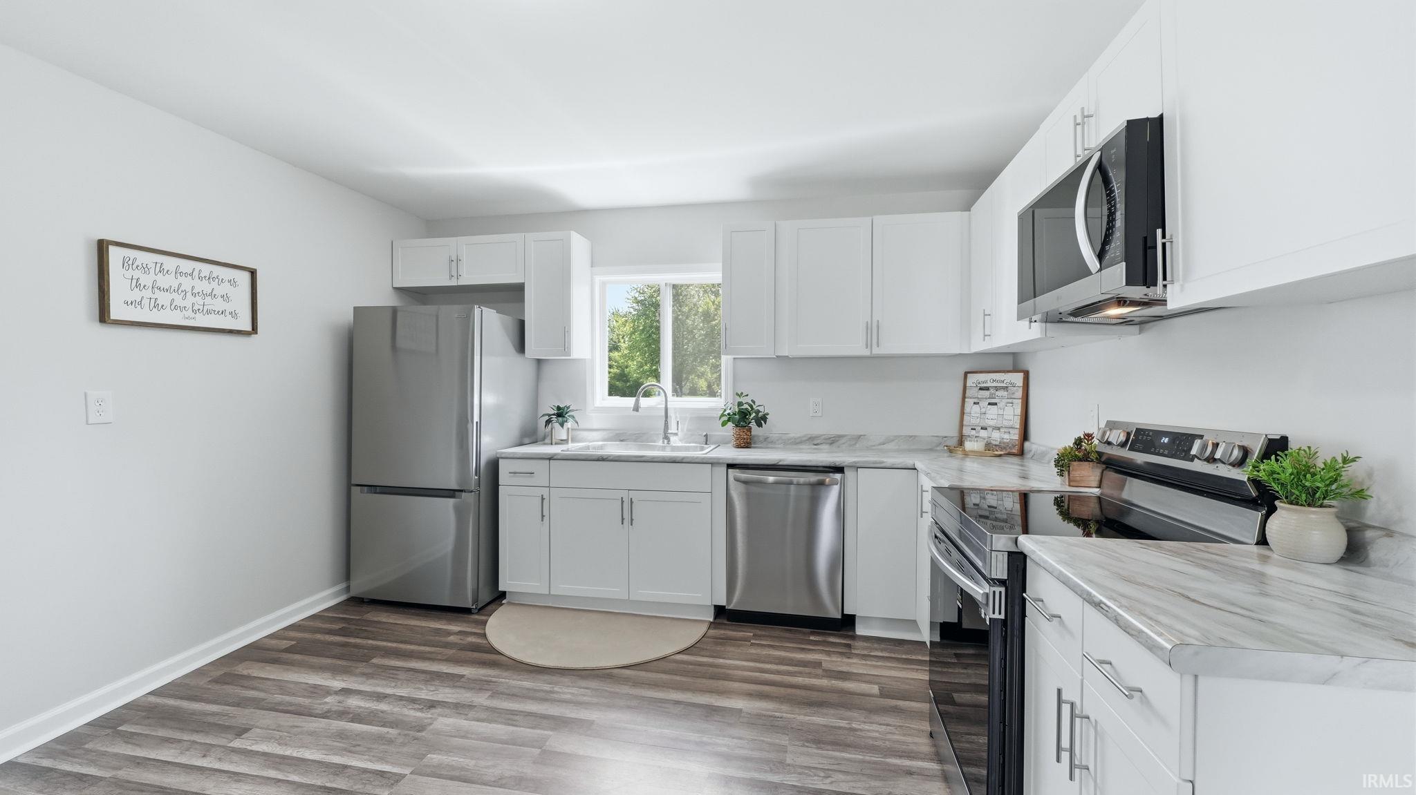 Modern kitchen featuring white cabinetry, stainless steel appliances, wood-finish flooring, and light-toned countertops