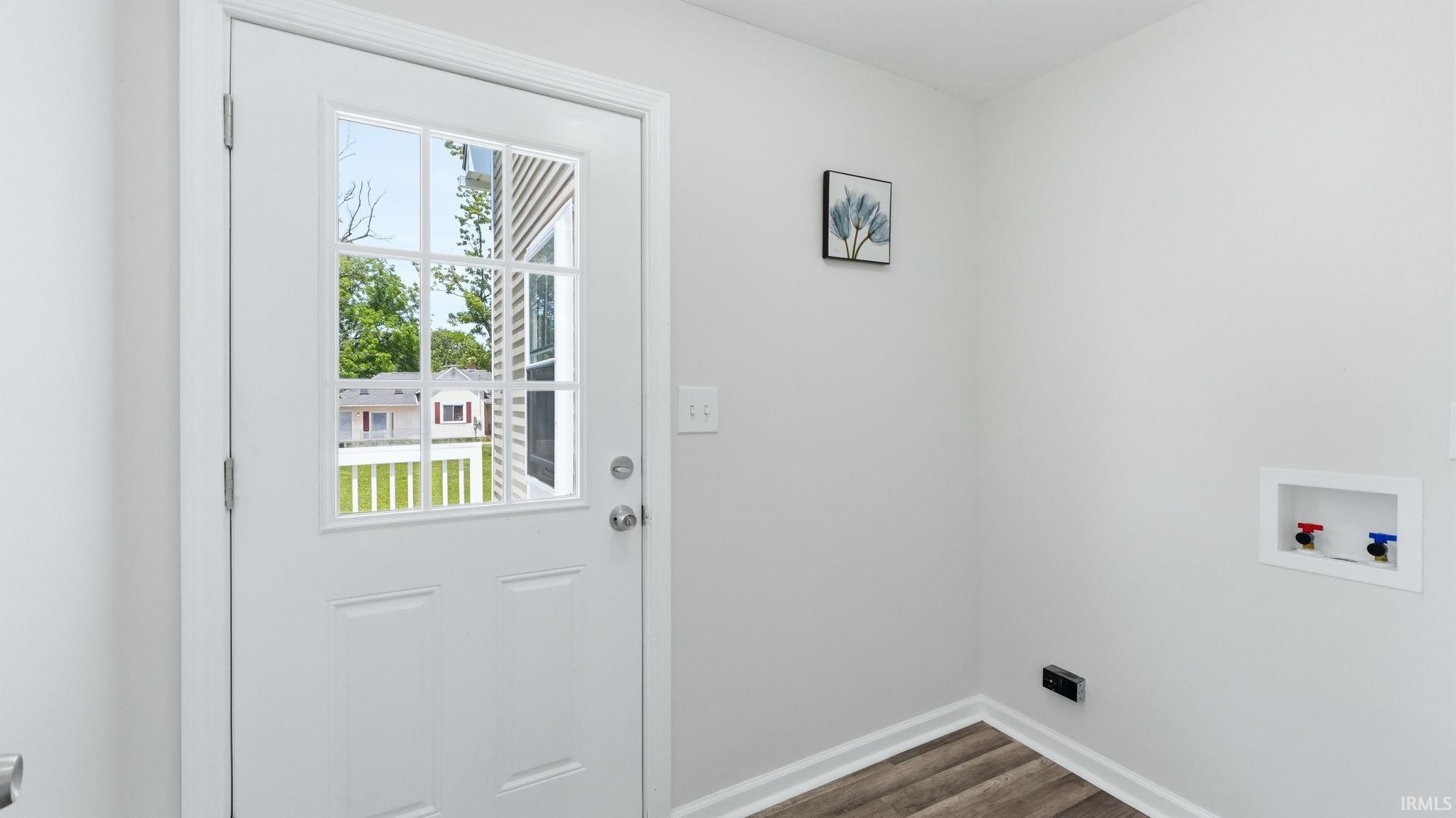 White paneled door with divided light window, wood-finish flooring, and recessed utility hookups