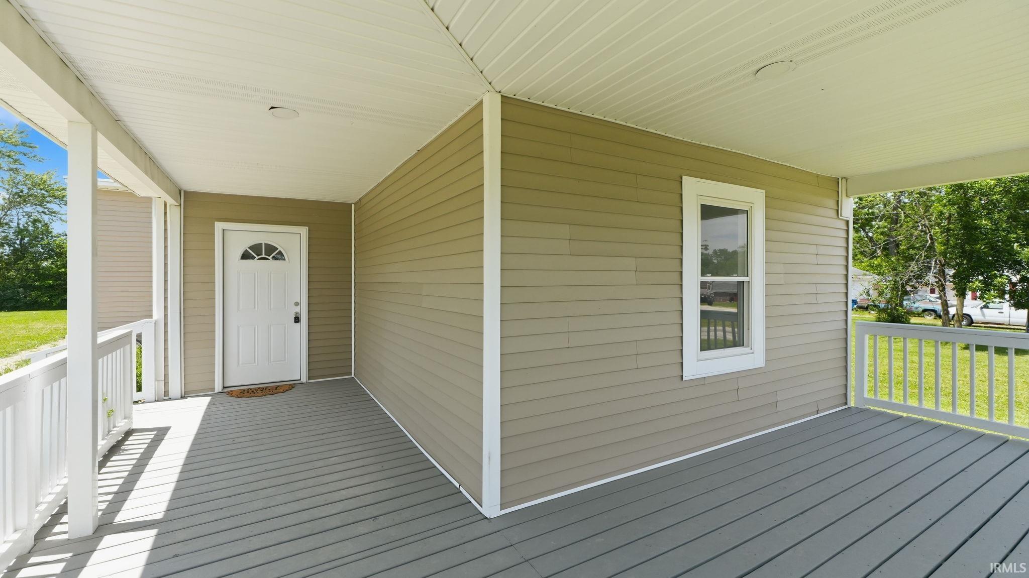 Covered front porch featuring a white entry door with a decorative fanlight, white railing, and grey deck flooring