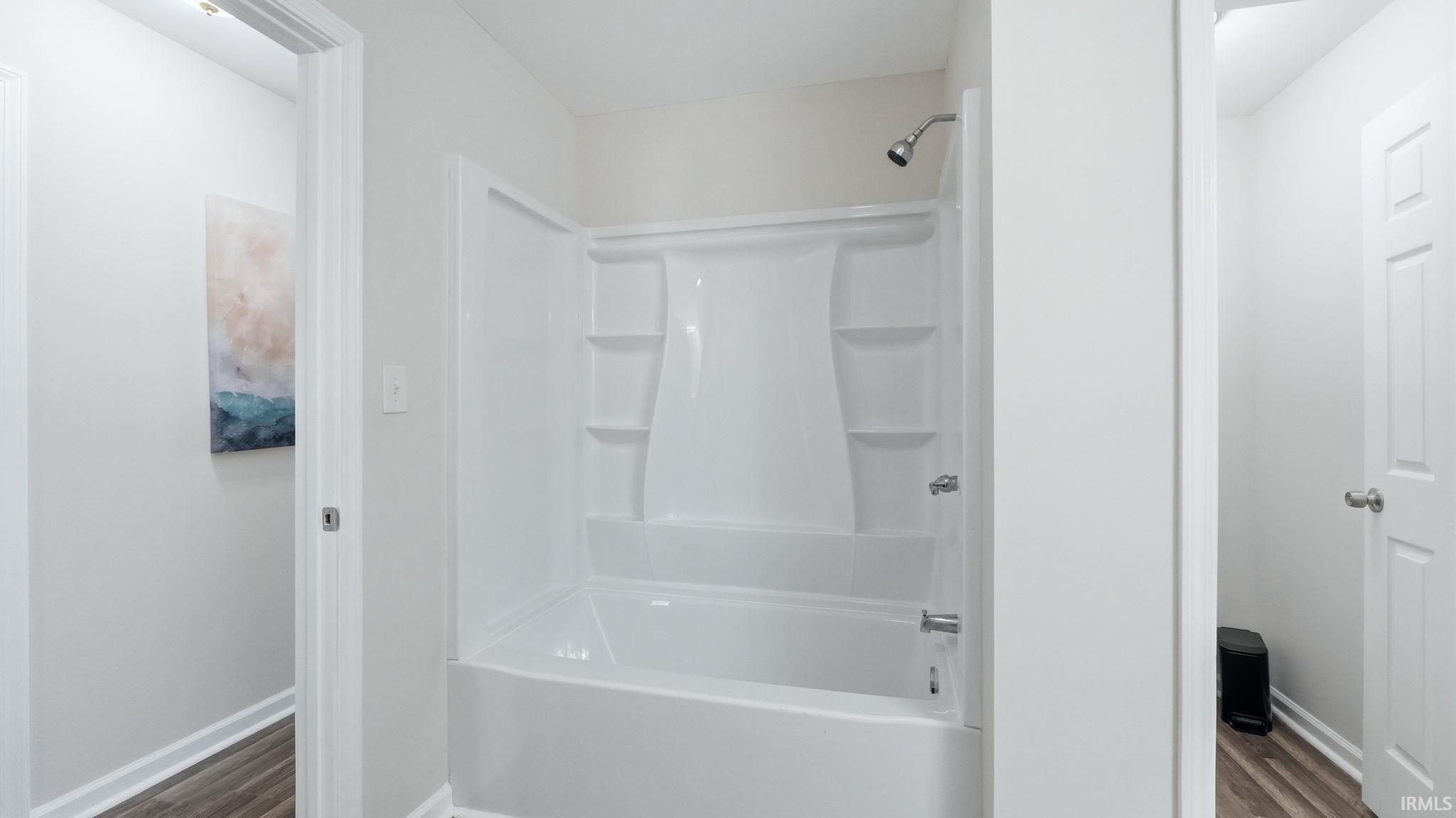 White bathtub with integrated shower, chrome showerhead, and integrated shelving