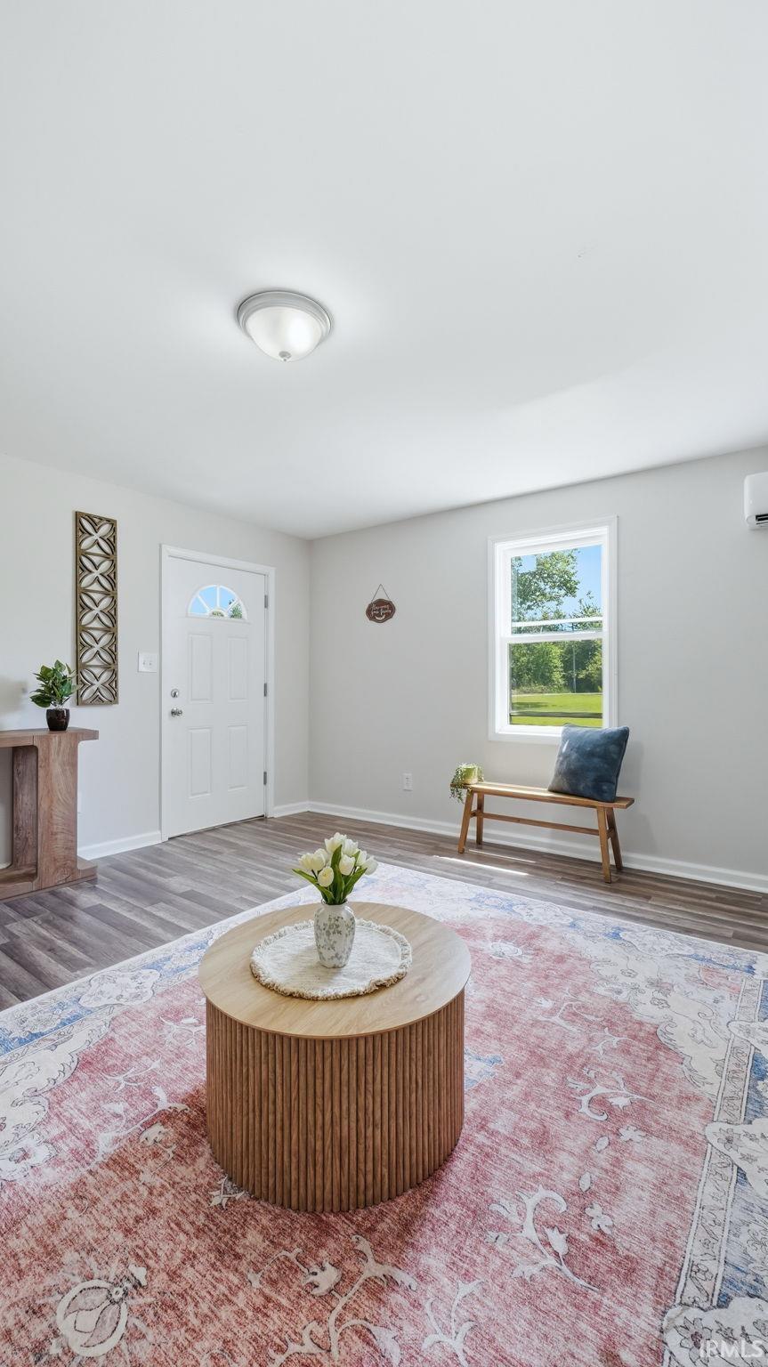 Inviting interior space featuring wood-finish flooring, light-colored walls, a prominent window, a white entry door, and a flush-mount ceiling light fixture