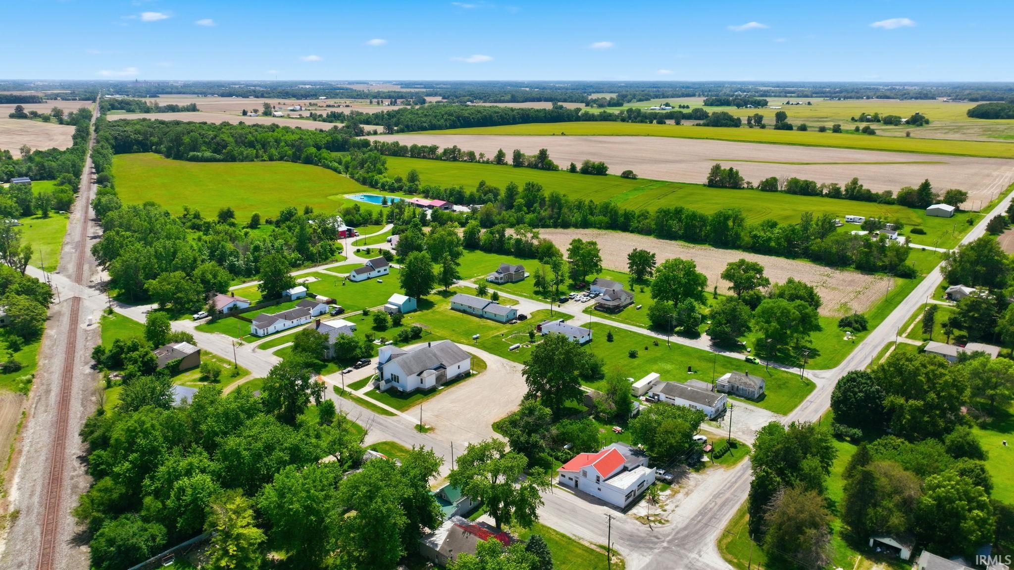 Aerial perspective showcasing a rural setting with residential properties, agricultural fields, and mature trees