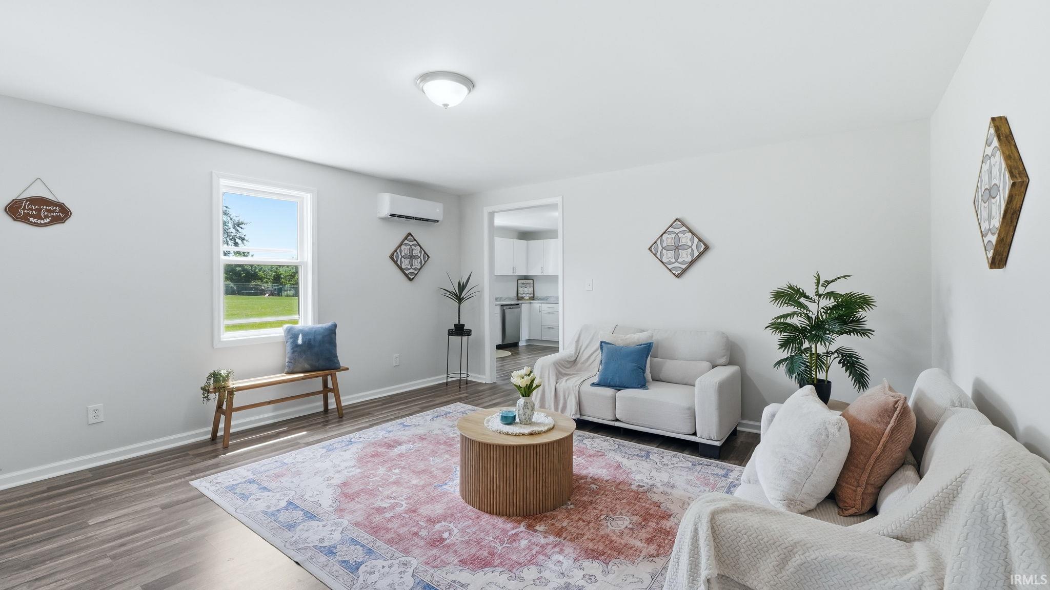 Spacious living area featuring light gray walls, wood-finish flooring, and a bright window overlooking a green expanse