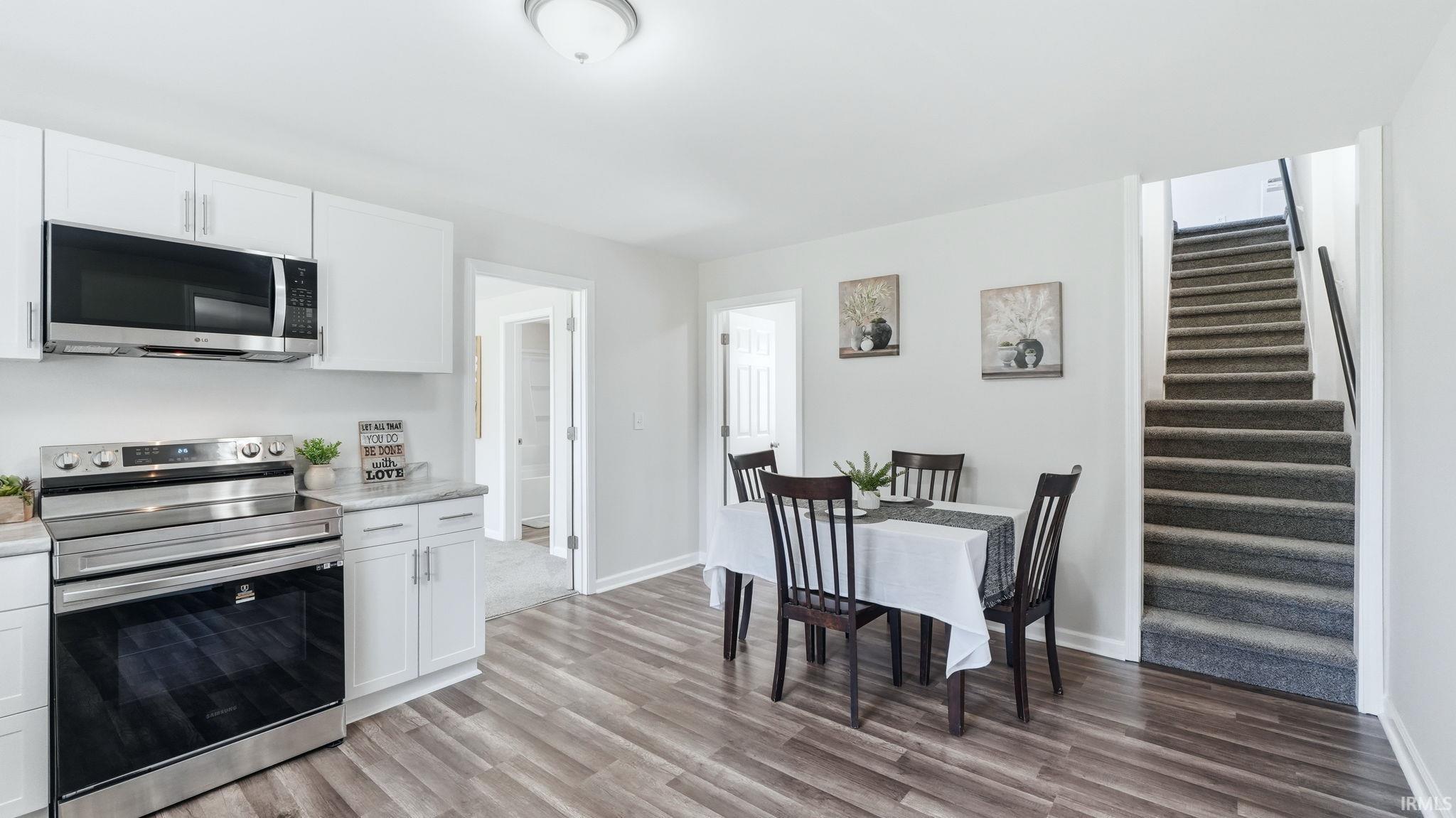 Kitchen and dining area featuring white cabinetry, stainless steel appliances, wood-finish flooring, and a carpeted staircase