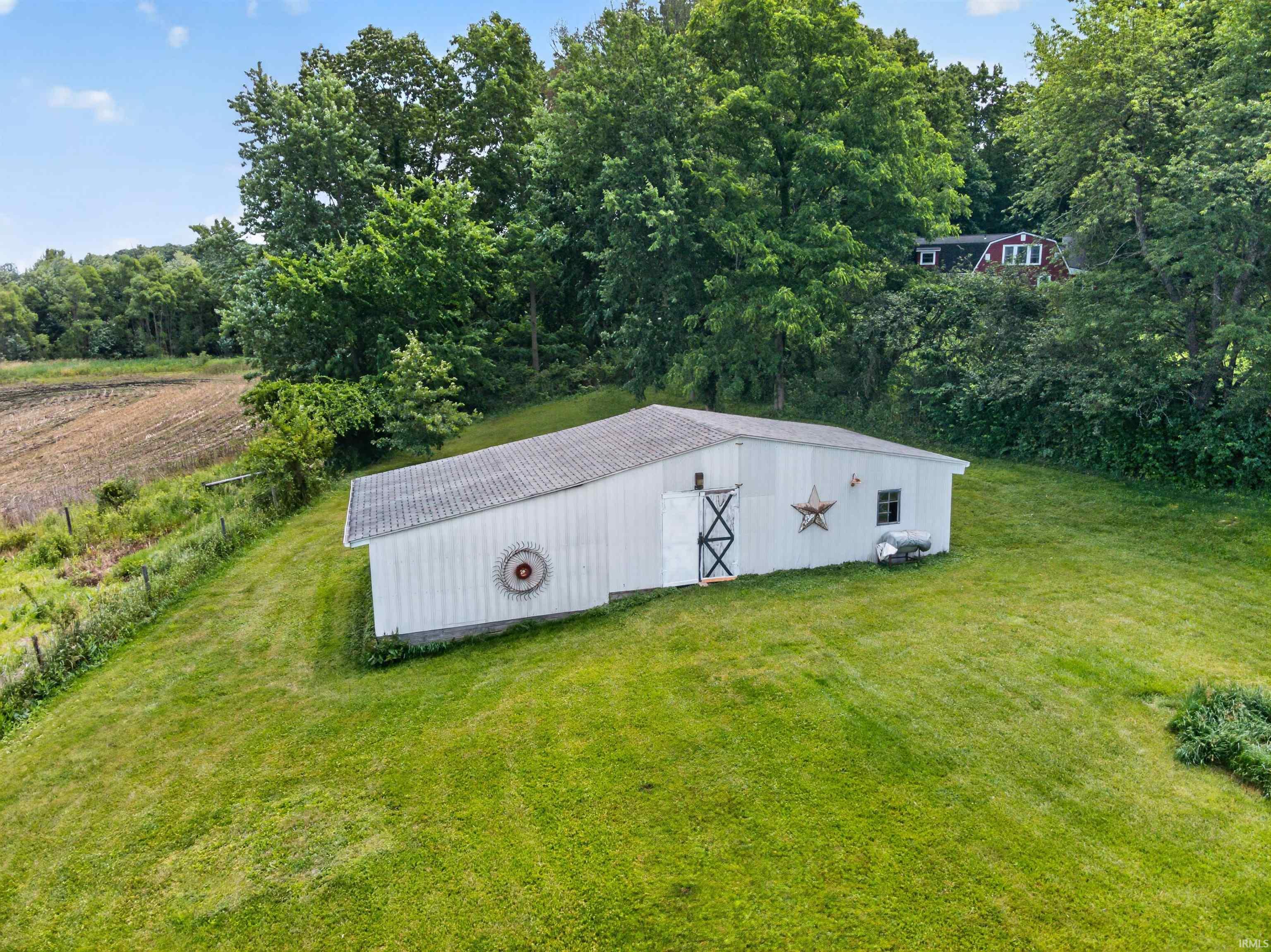 White-sided outbuilding with a gray roof, surrounded by expansive green lawn