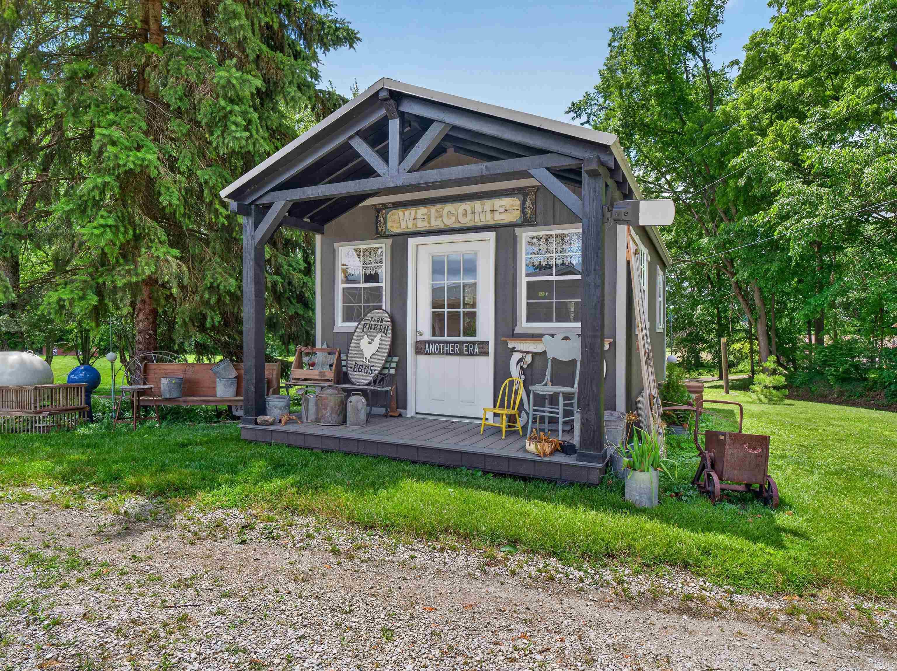 Detached outbuilding with a covered porch, white entry door, two windows, and a dark exterior finish