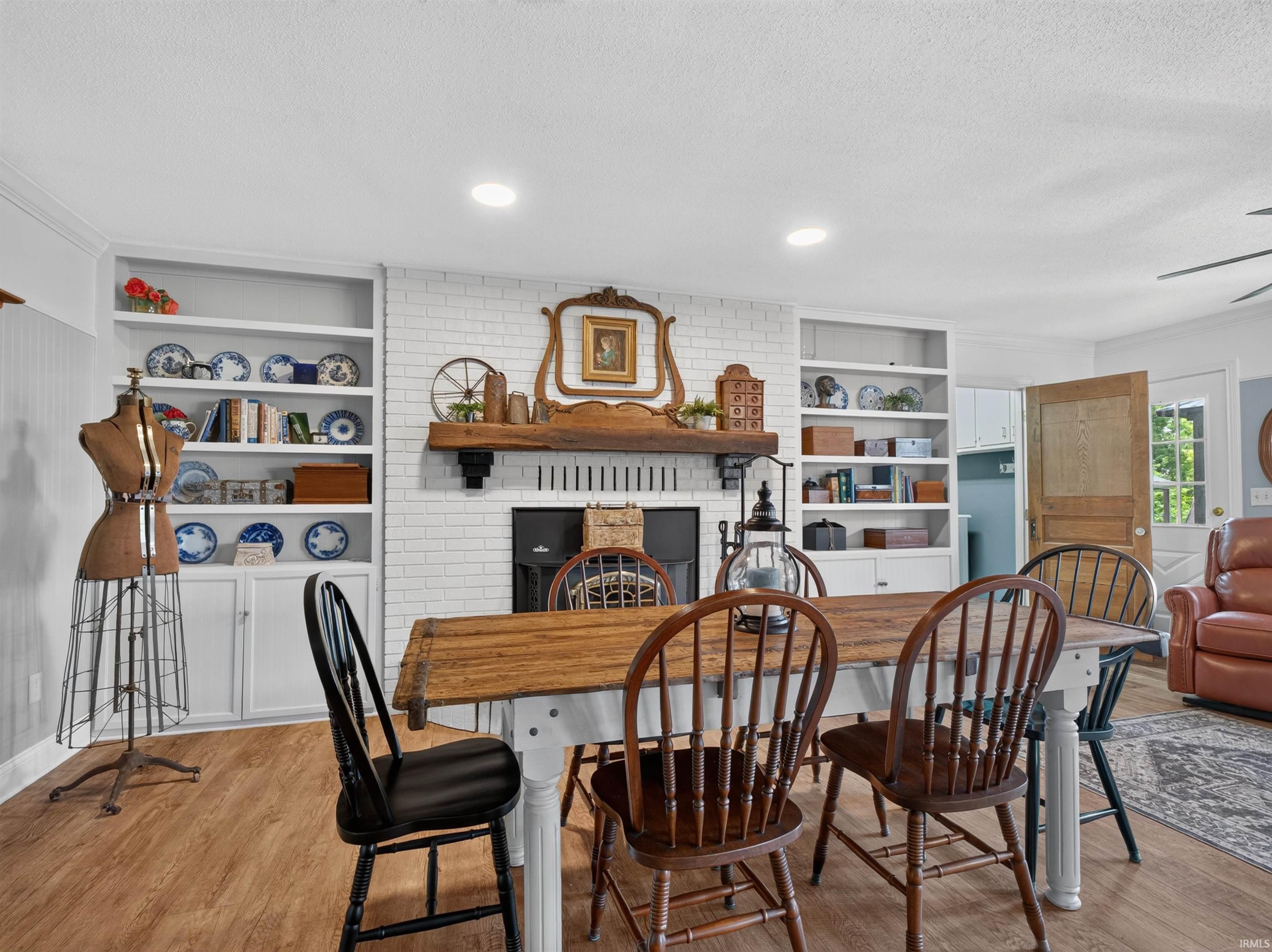 Dining space featuring wood-finish flooring, a white brick fireplace with a wood mantle, recessed lighting, and built-in shelving