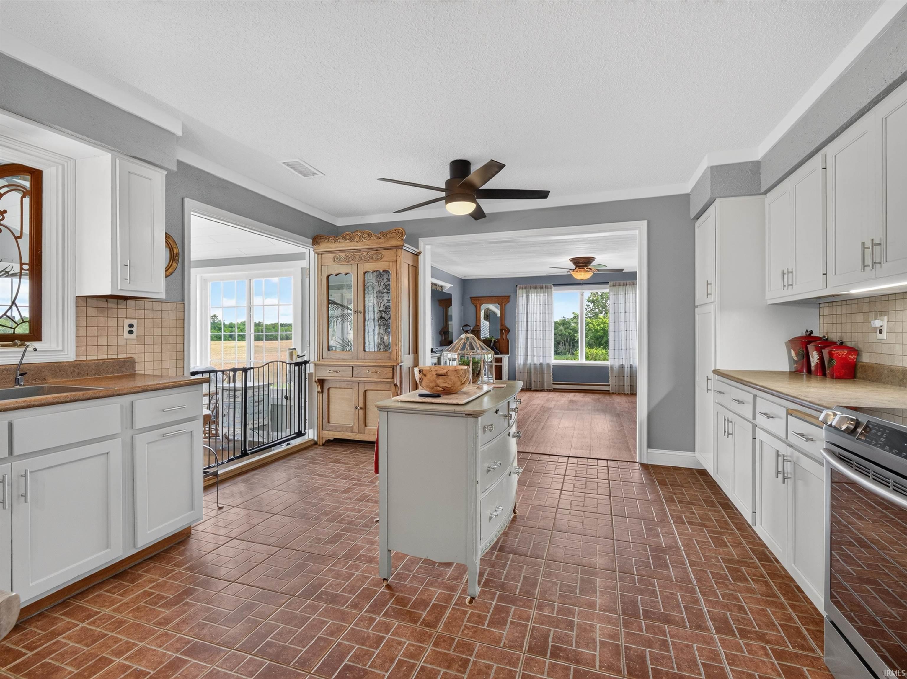 Kitchen featuring brick-patterned tile flooring, white cabinetry, light-toned countertops, and a tiled backsplash