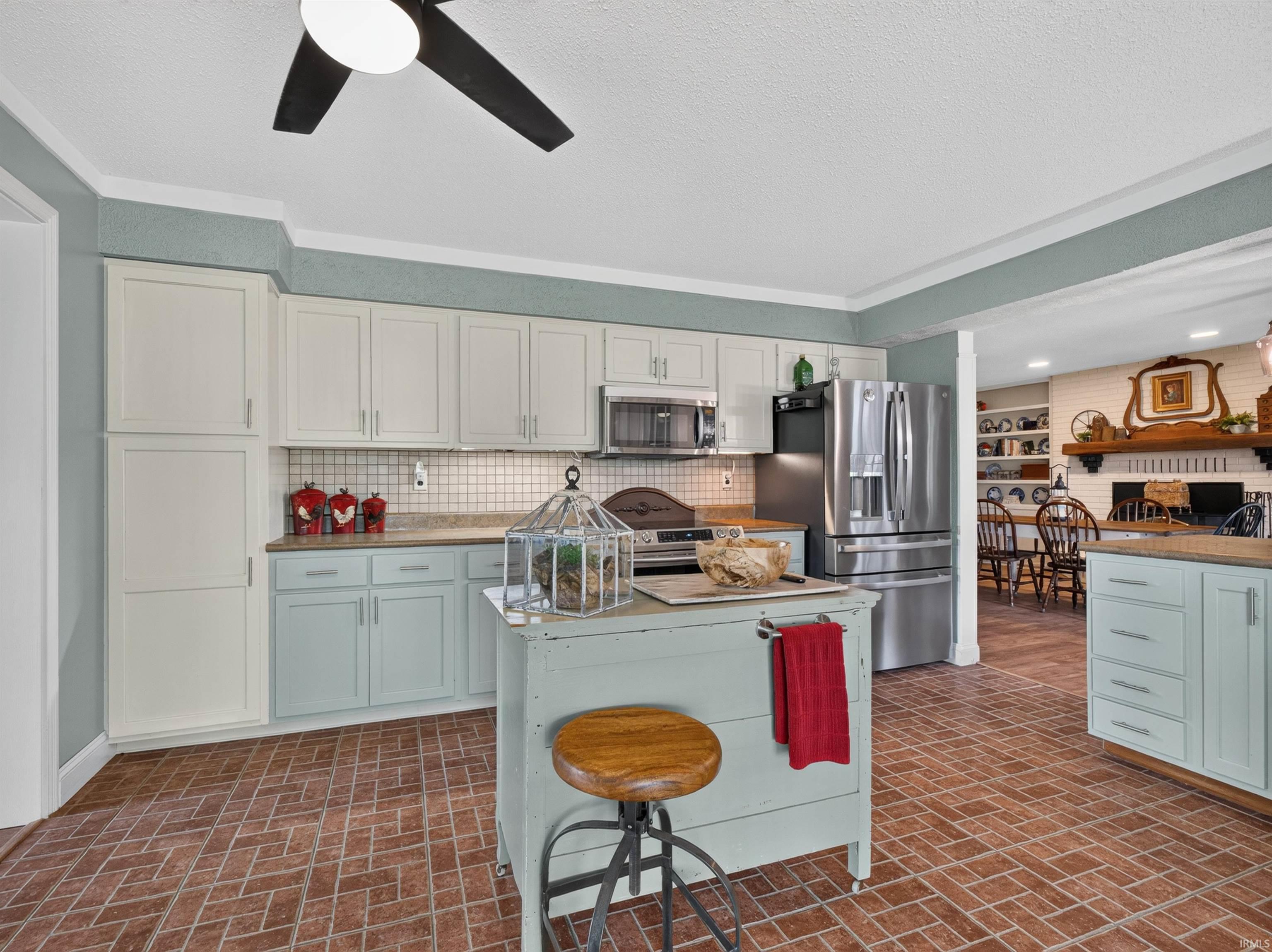 Kitchen featuring brick-pattern flooring, two-tone cabinetry, stainless steel appliances, a tile backsplash, and a central island