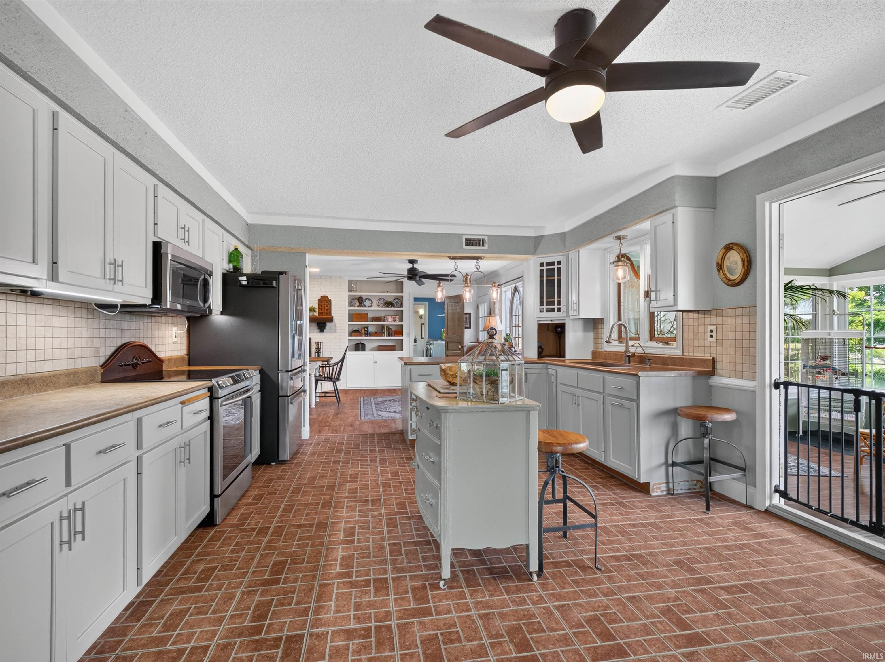Kitchen featuring brick flooring, perimeter cabinetry, a central island, stainless steel appliances, and a tile backsplash