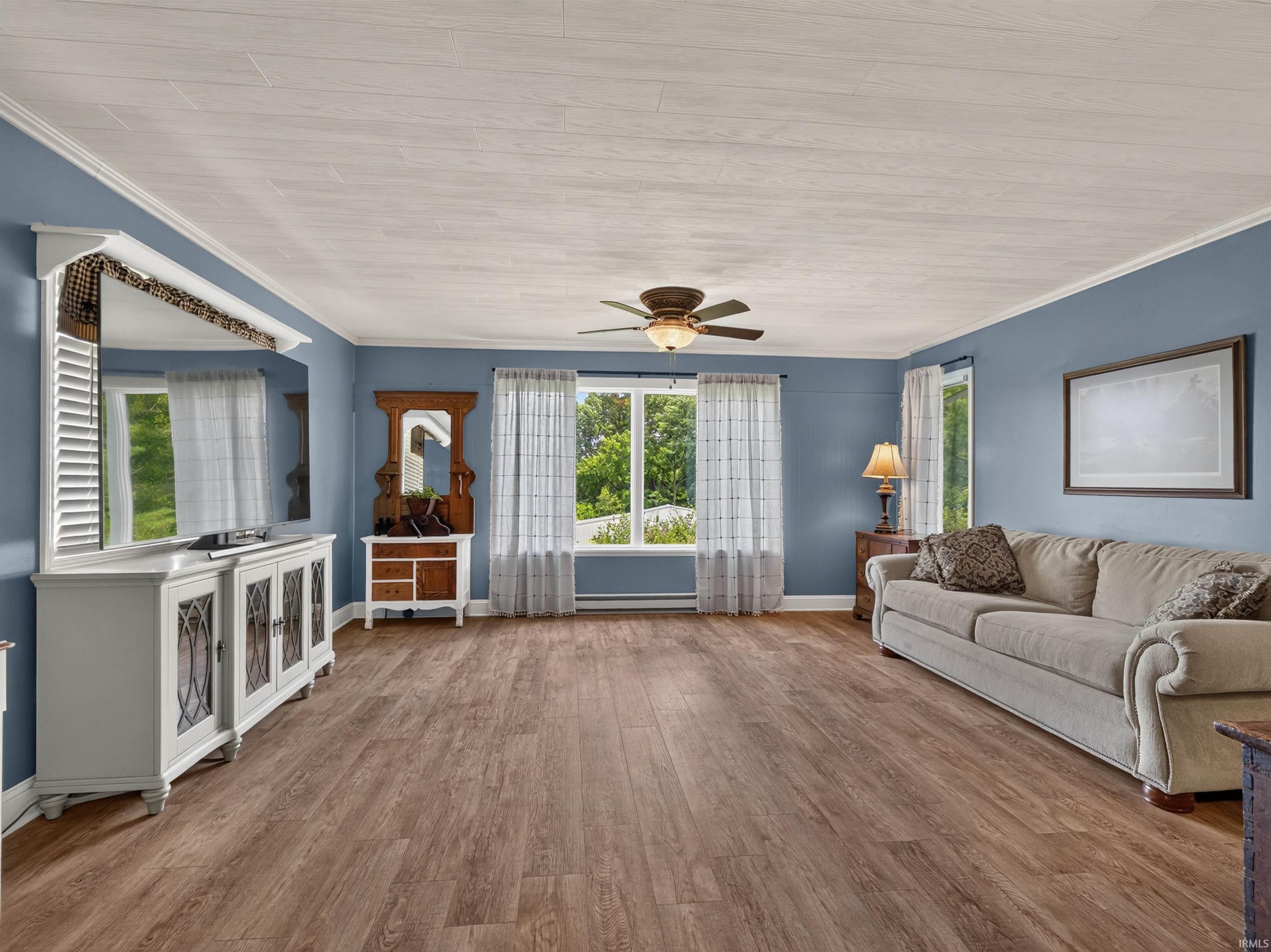 Spacious interior featuring wood-finish flooring, light blue wall paint, multiple windows, and a ceiling fan
