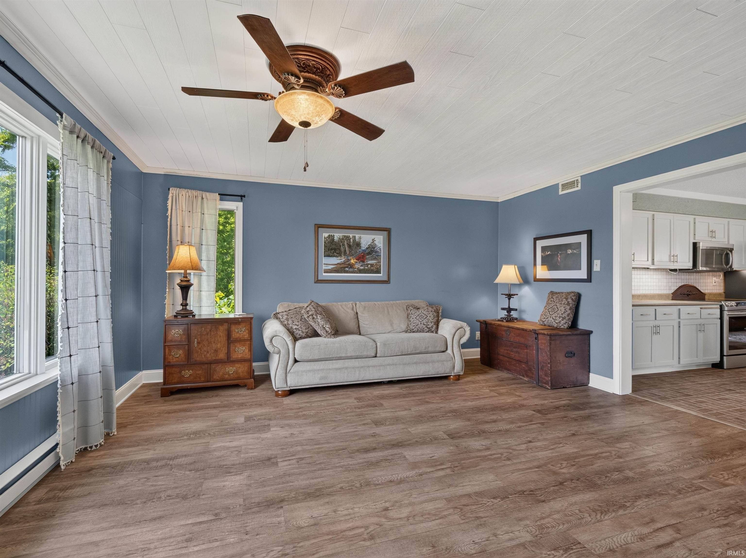 Spacious living area featuring wood-finish flooring, a ceiling fan with integrated lighting, and multiple windows