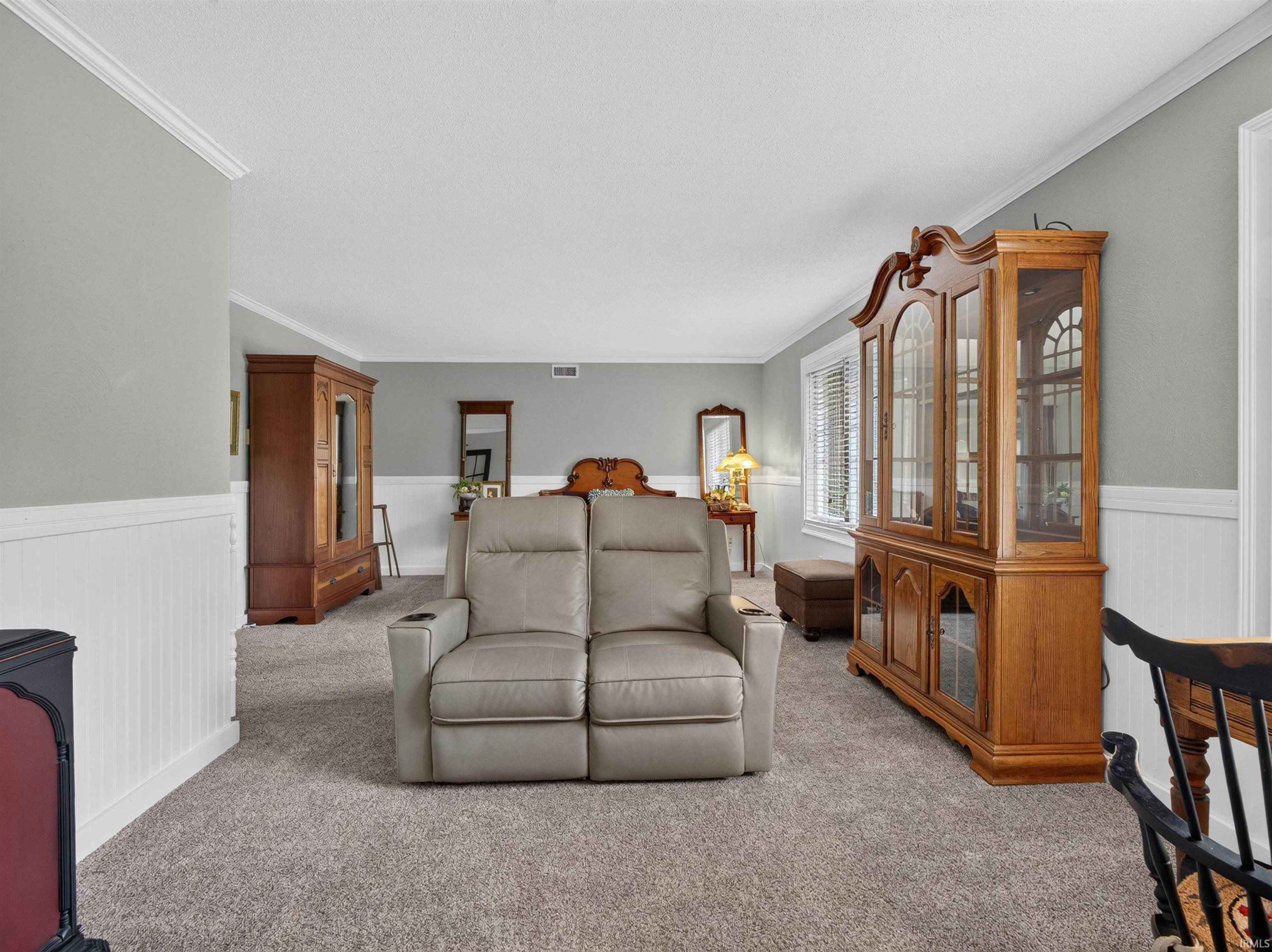 Carpeted living space featuring wainscoting and crown molding
