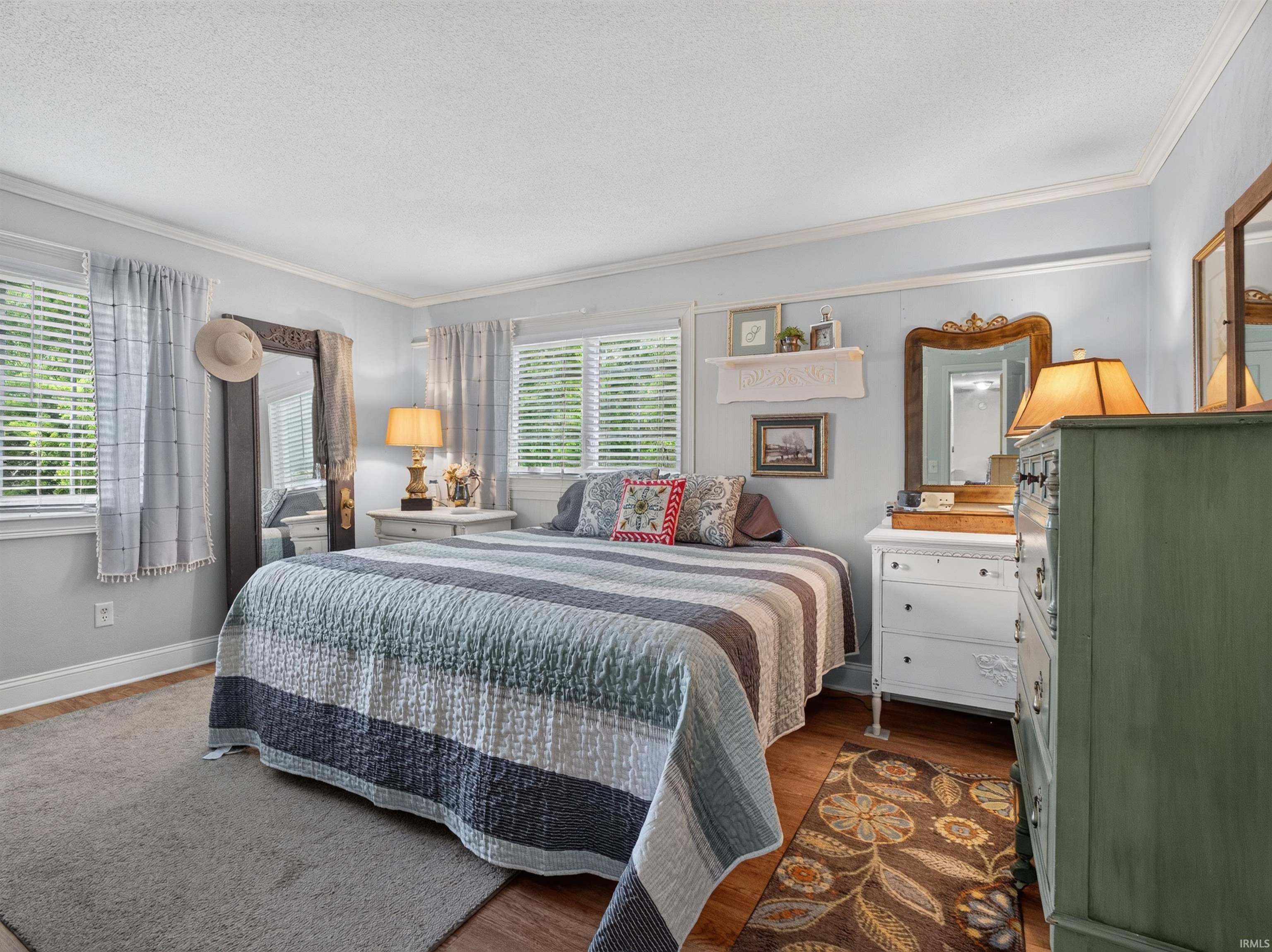 Bright bedroom featuring multiple windows, crown molding, a combination of wood-finish flooring and carpet, and light blue wall tones