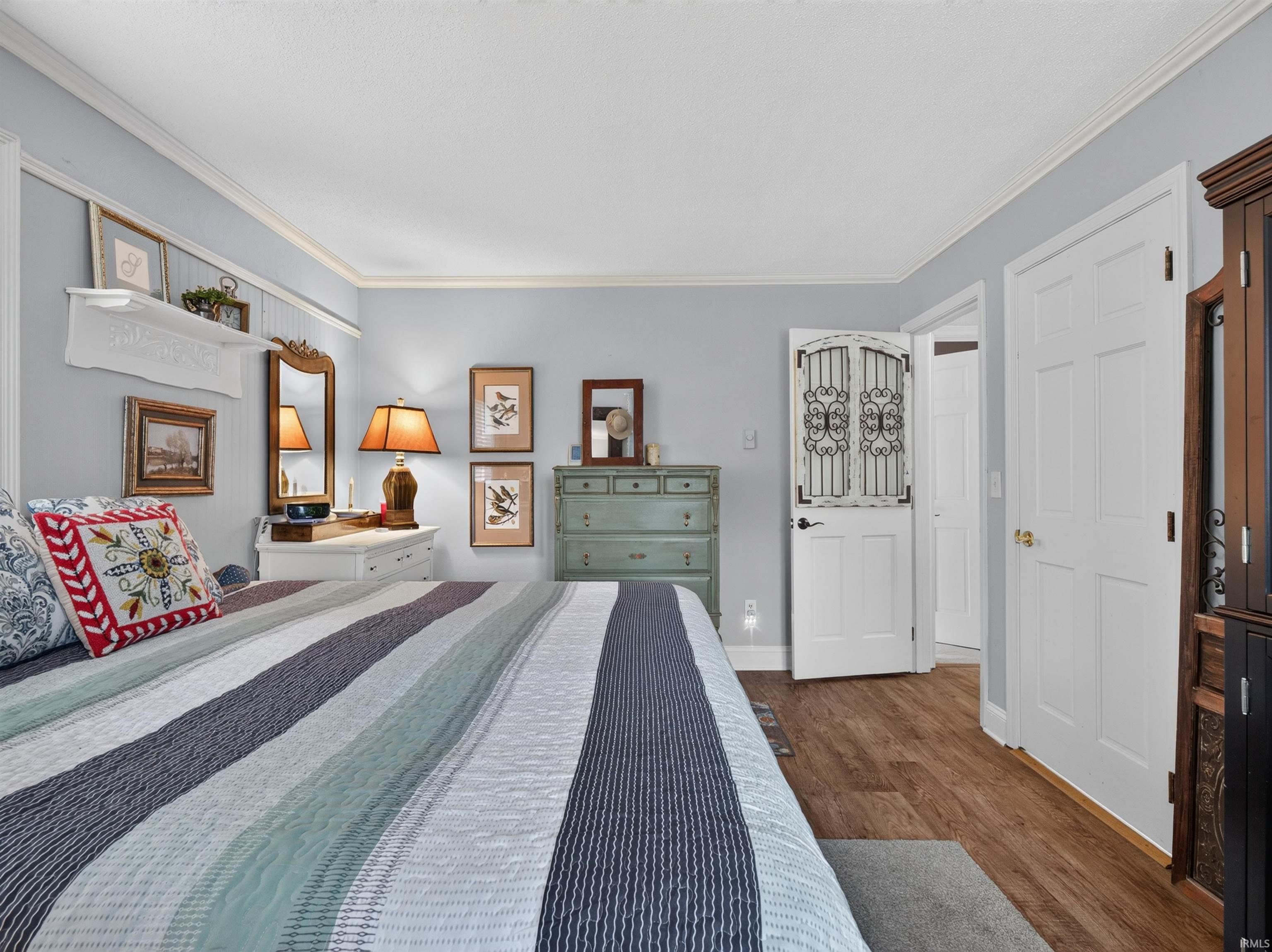 Spacious room featuring wood-finish flooring, light blue wall paint, white crown molding, and two white panel doors