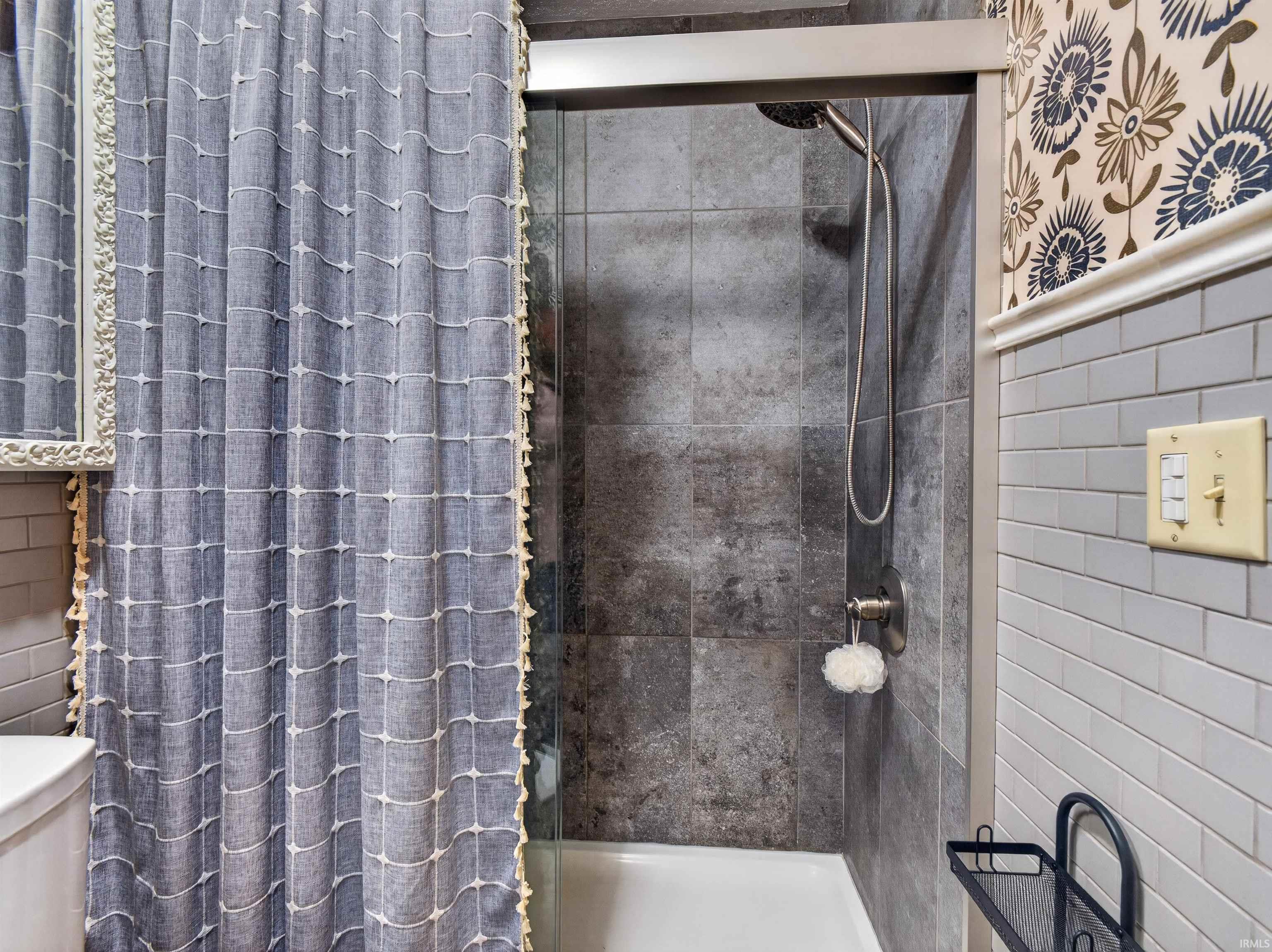 Shower enclosure with dark large-format tile surround, brushed nickel fixtures, and a glass panel
